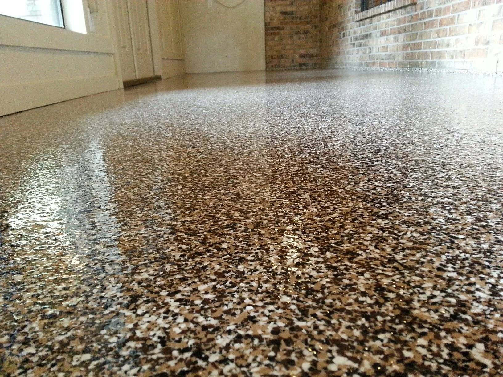 Close-up view of a polished, flake epoxy or terrazzo floor in a room with brick wall, white cabinets, and a glass door.