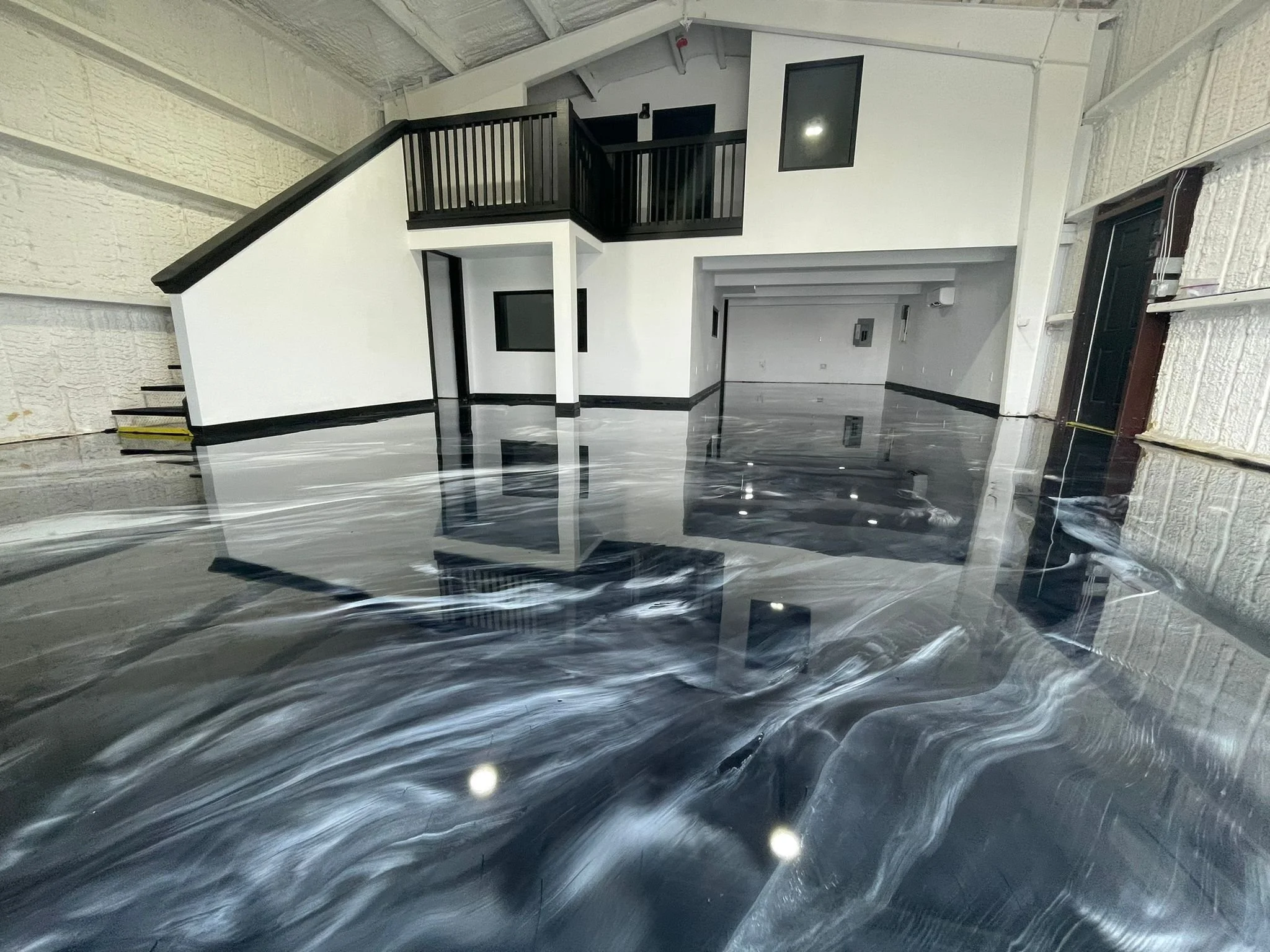 Interior view of a building under construction with glossy black and white marble custom epoxy flooring, white walls with black trim, and an open space with an upper balcony.