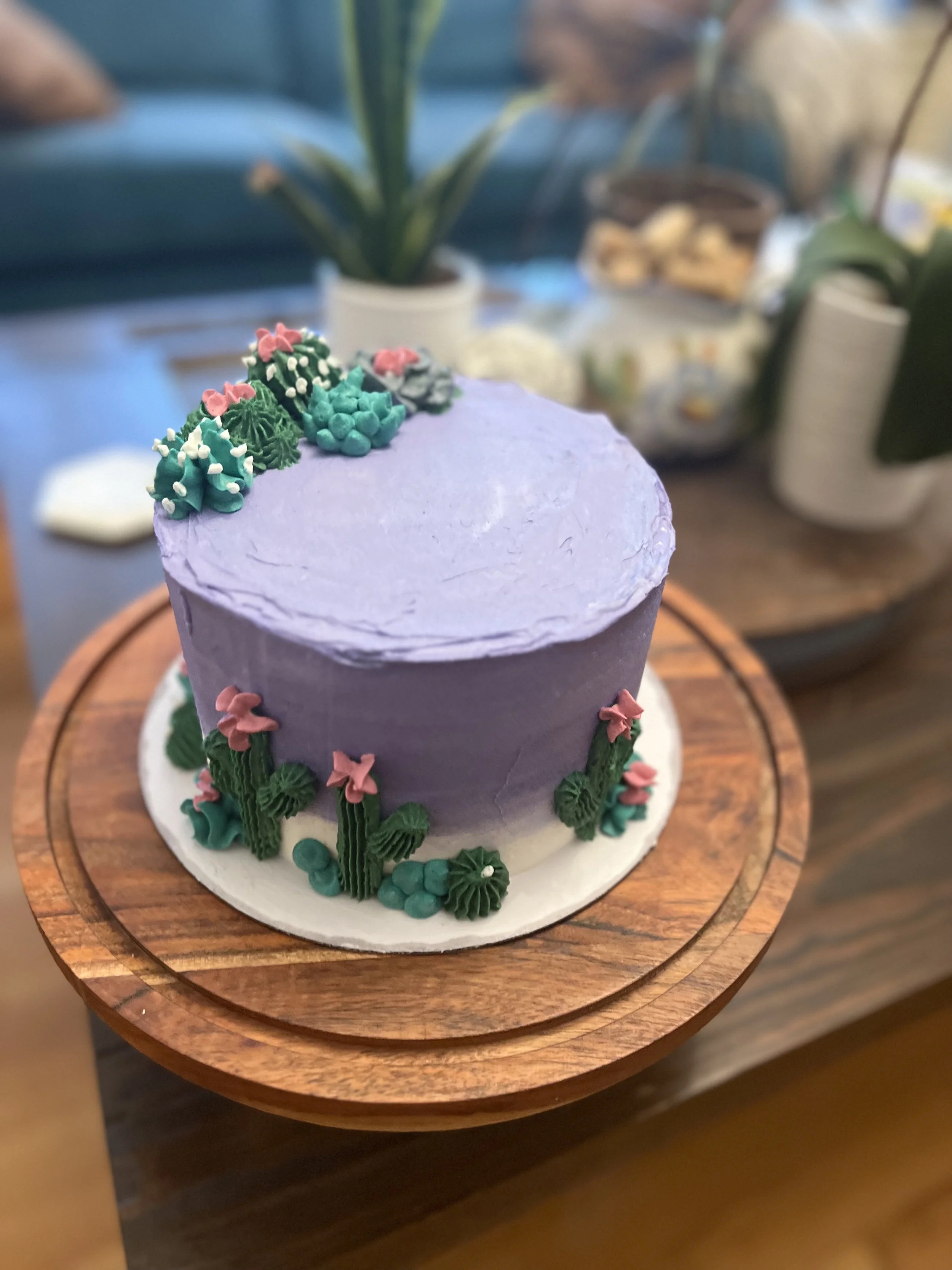 Lavender-colored cake with cactus and flower decorations on top and around the sides.