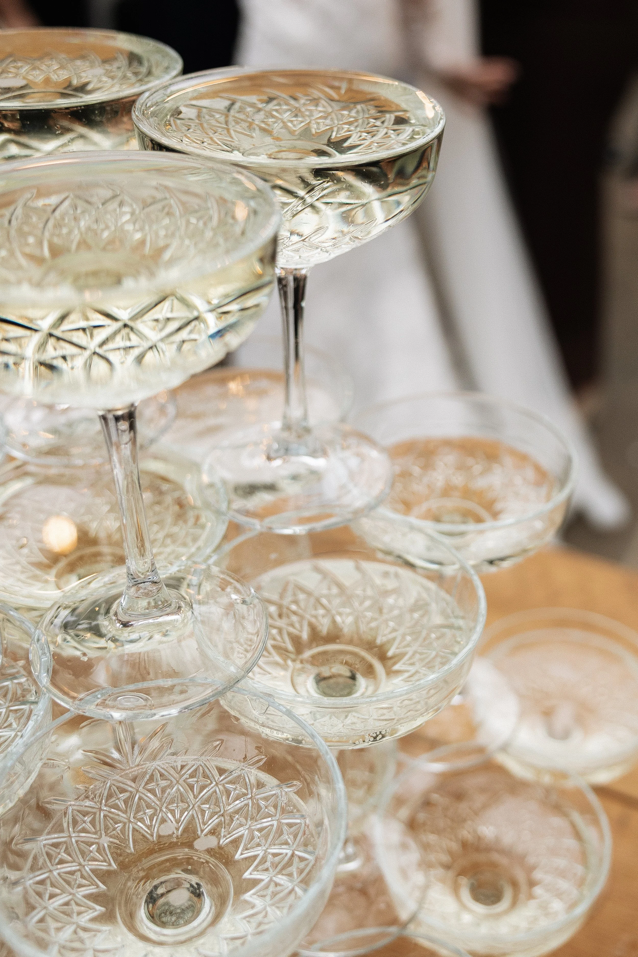 Glass coupe and coupe with intricate patterns filled with a clear liquid, arranged in a pyramid on a table.