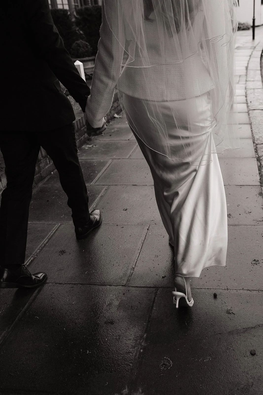A bride and groom holding hands walking on a sidewalk near a church or building.