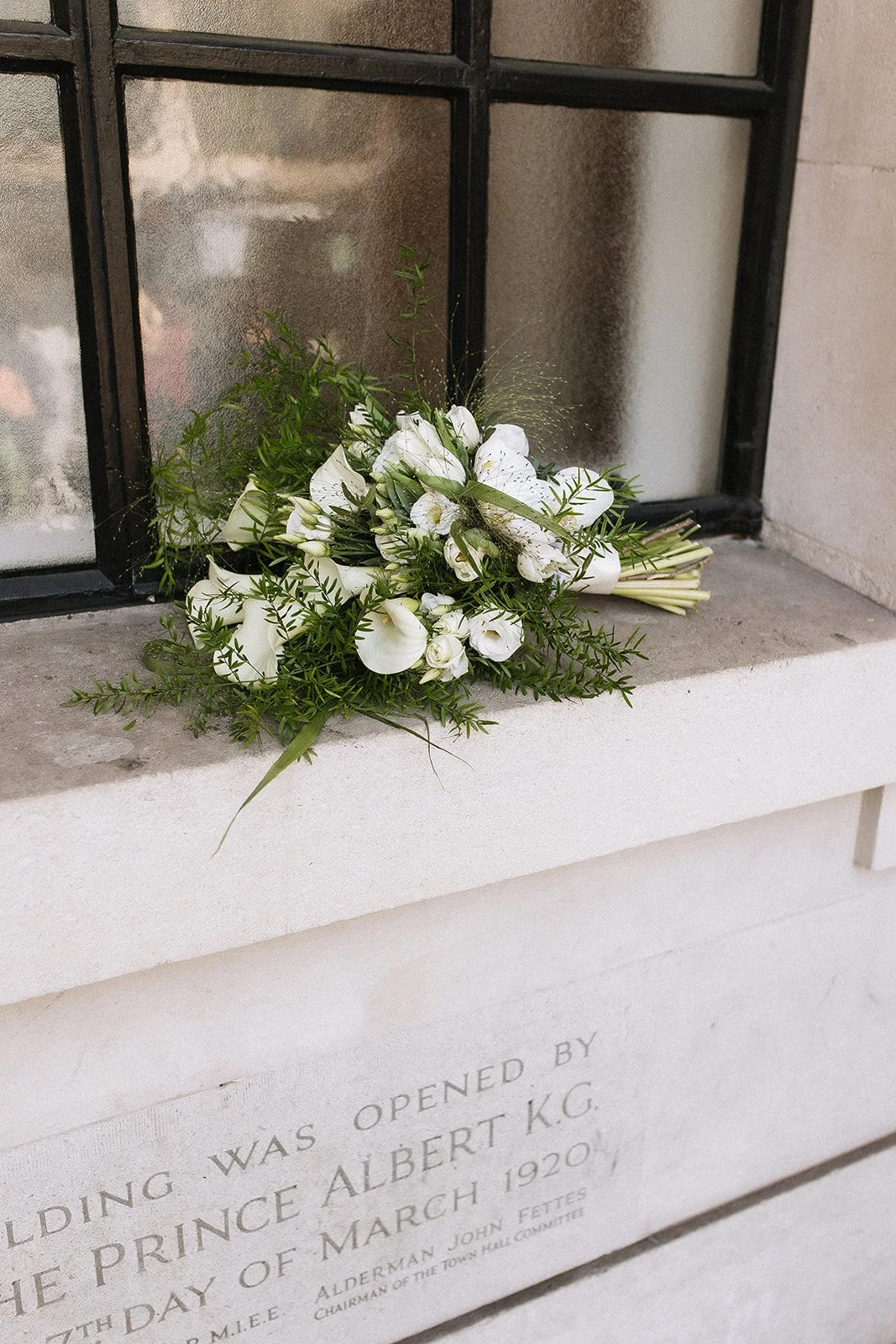 A bouquet of white flowers resting on a stone ledge in front of a memorial plaque at The Old Marylebone Town Hall in London.