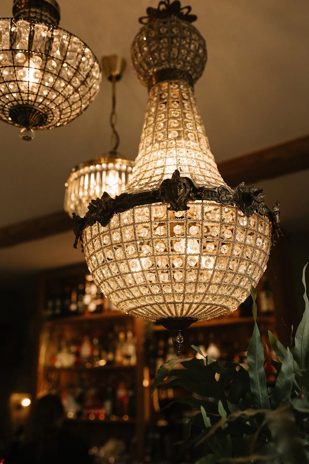 An ornate chandelier with glass crystals and decorative metalwork hanging from the ceiling, casting warm light in a cozy room.