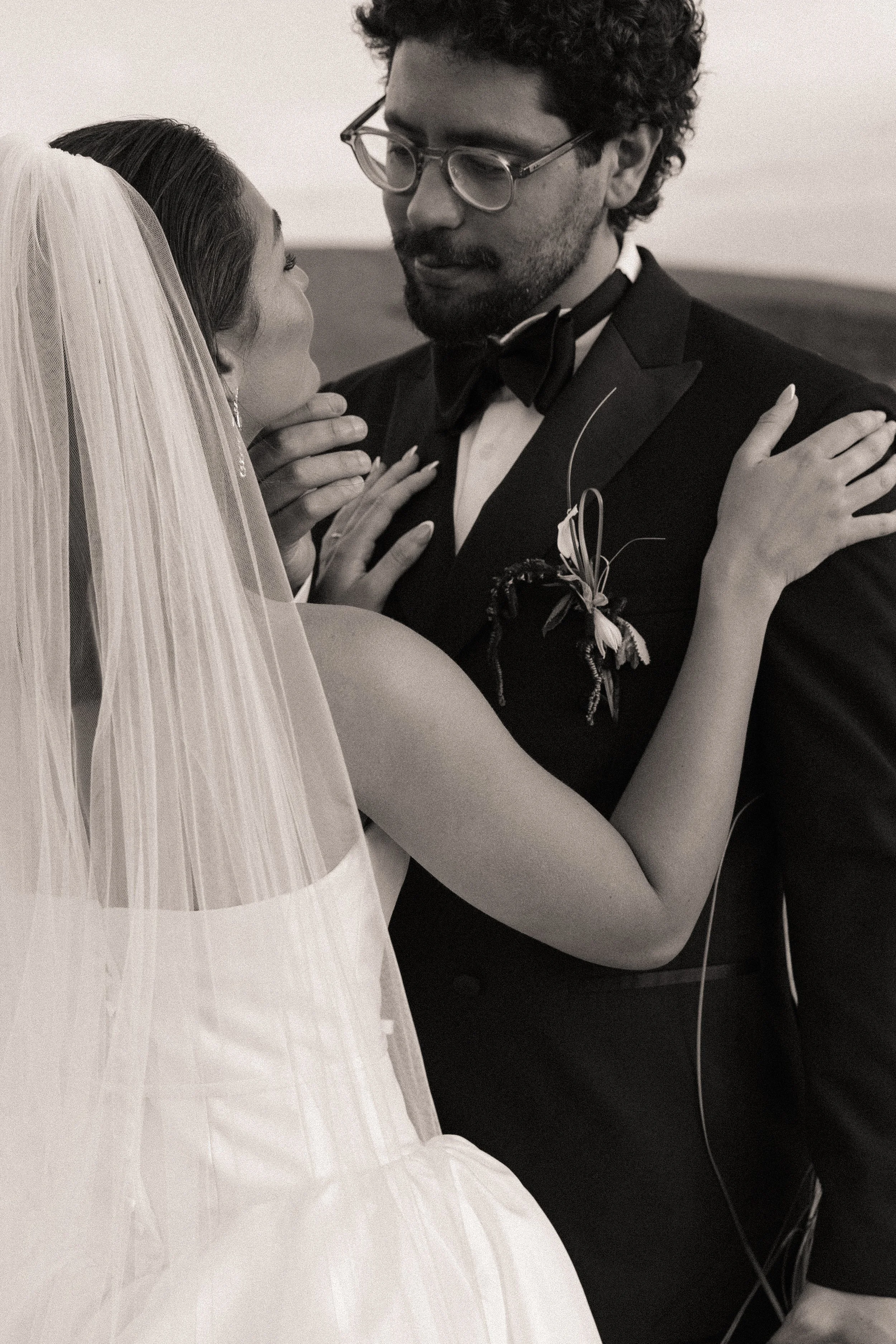 A bride and groom sharing a romantic dance at their wedding, with the bride wearing a wedding dress and veil, and the groom in a tuxedo with glasses.