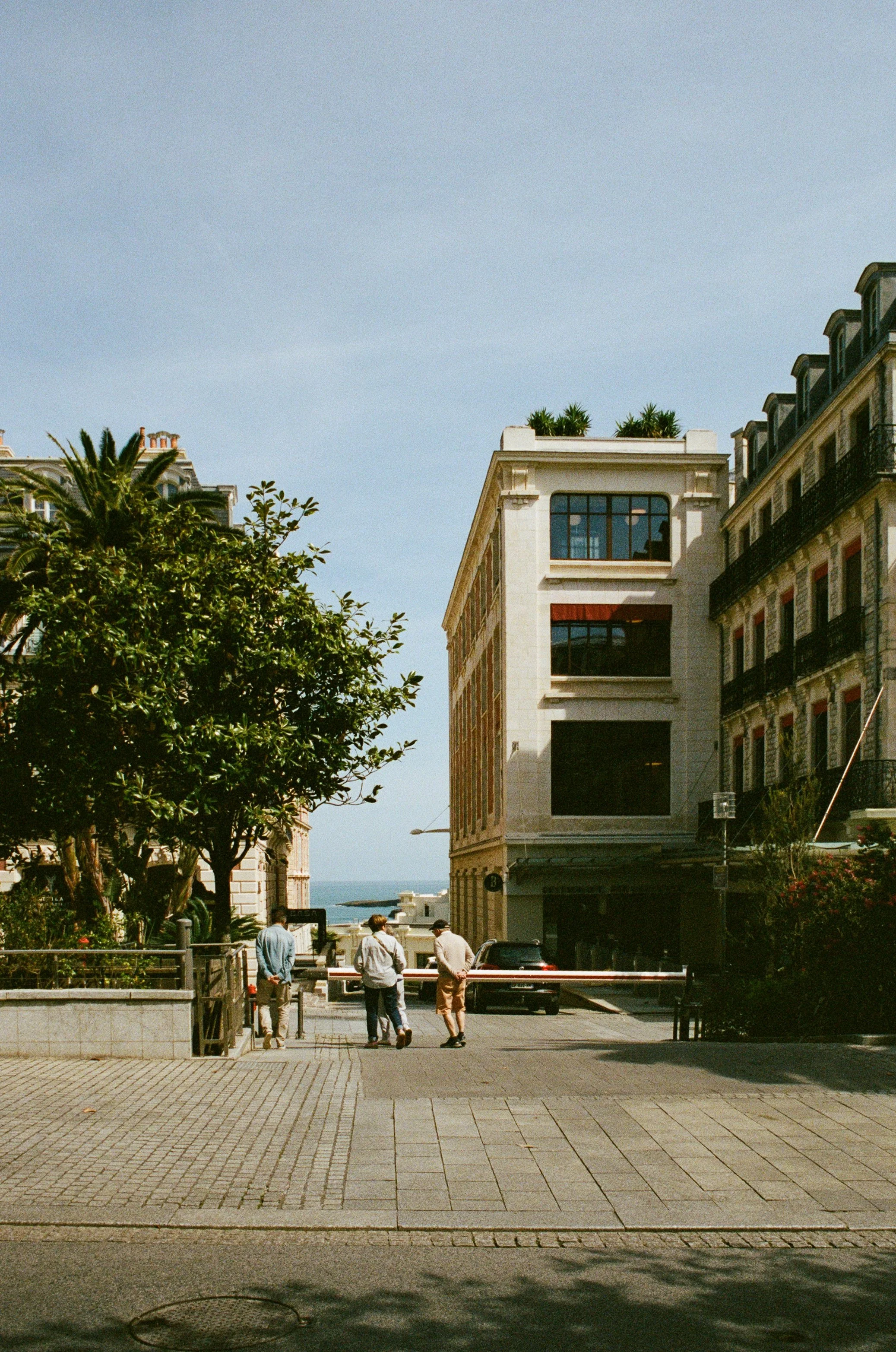 Urban street scene with pedestrians, a vintage car, trees, and buildings in the background.