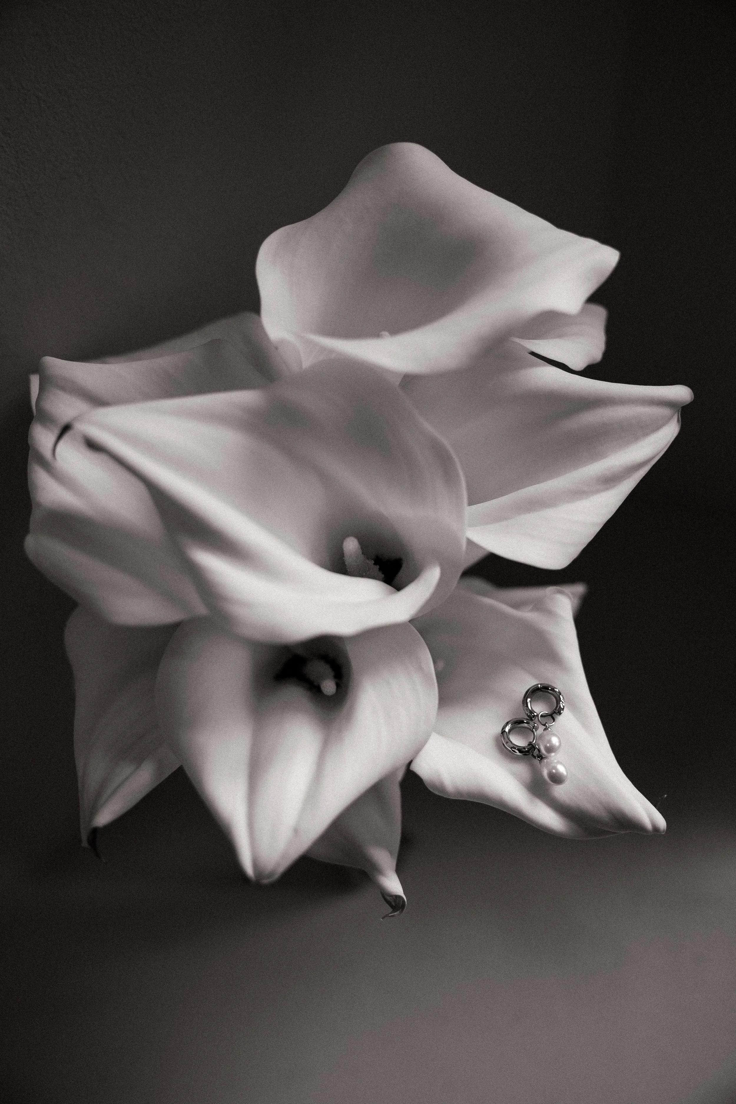 Close-up of white lilies and calla lilies with jewelry, including pearl earrings, on a dark background.