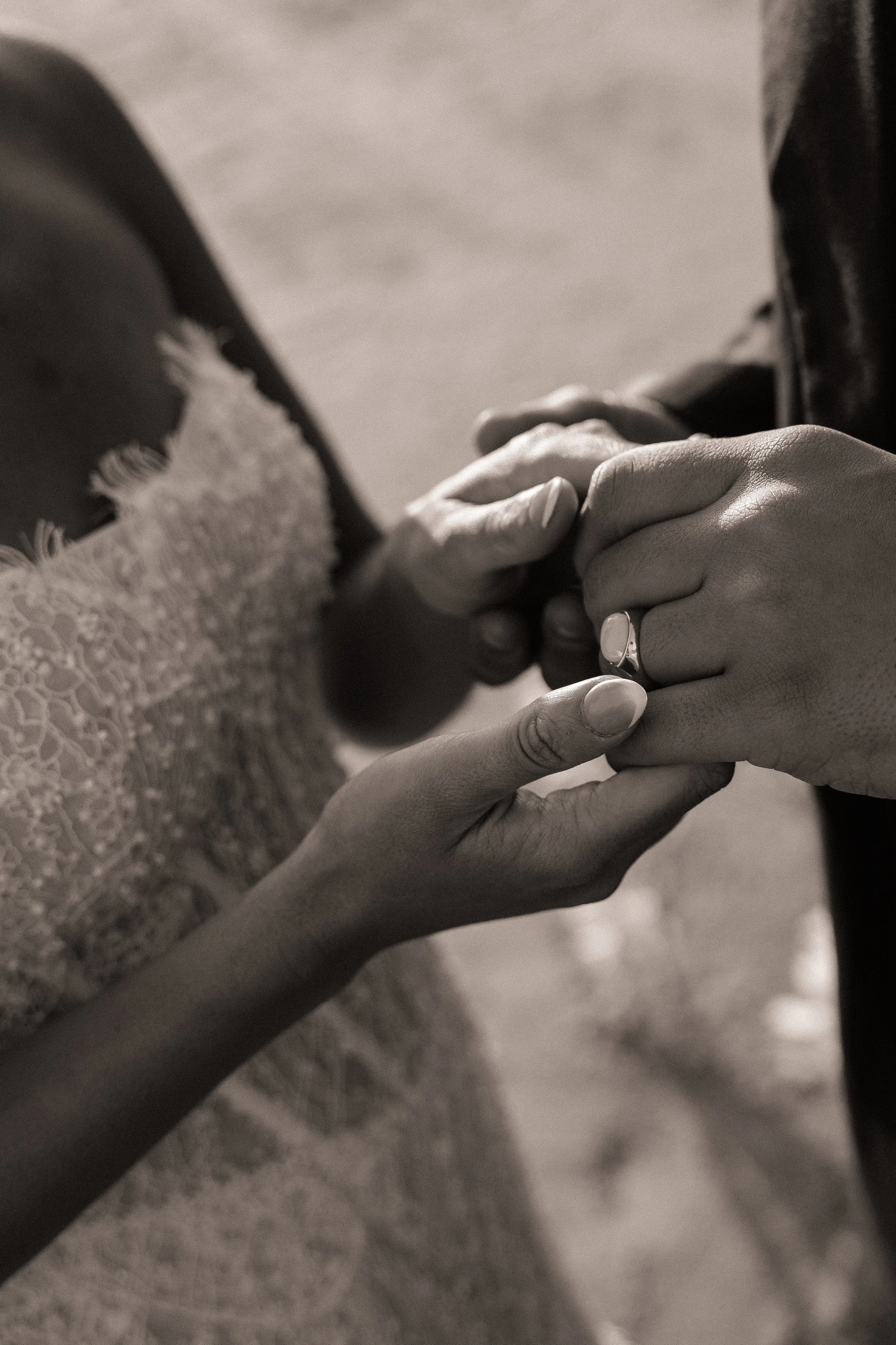 Close-up of two people holding hands, one person with a wedding ring and lace sleeve, the other person's hand gently grasping the first person's fingers.