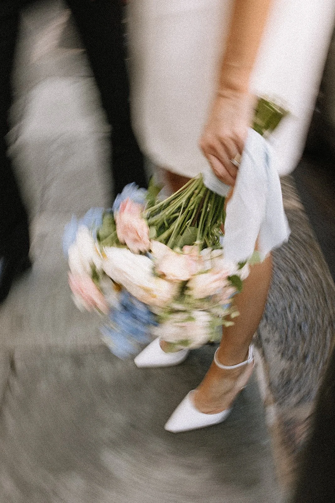 Person holding a bouquet of pink and white flowers in a wedding dress and white heels.
