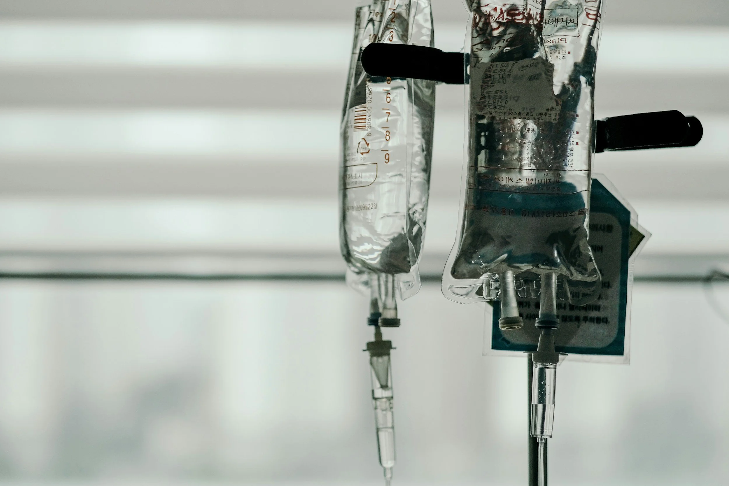 Medical IV bags hanging from an IV pole in a clinical setting.