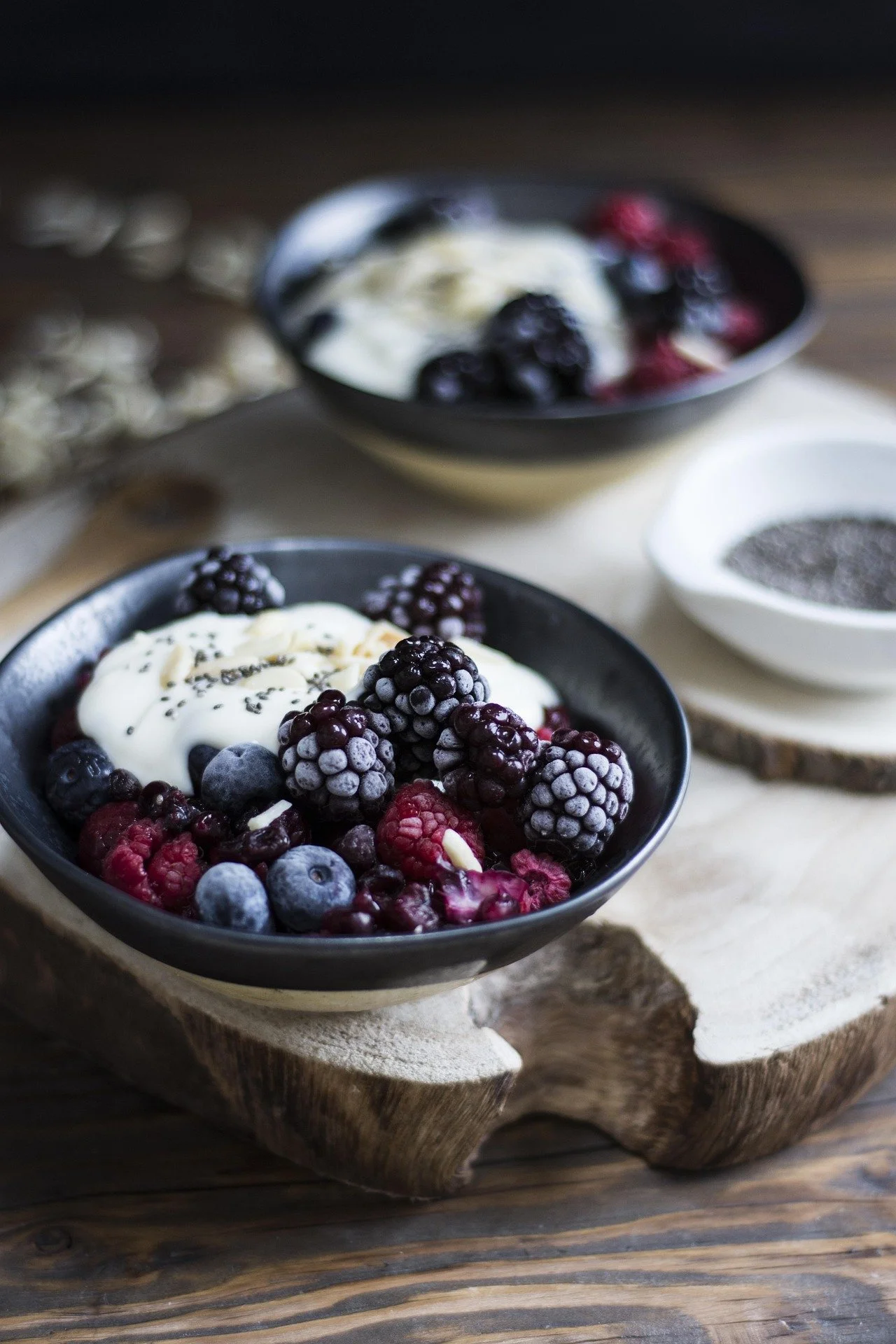 A bowl of mixed berries topped with cream and chia seeds on a rustic wooden surface.
