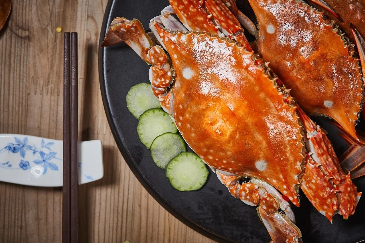 Cooked crabs on a black plate with cucumber slices on the side, wooden table and chopsticks.