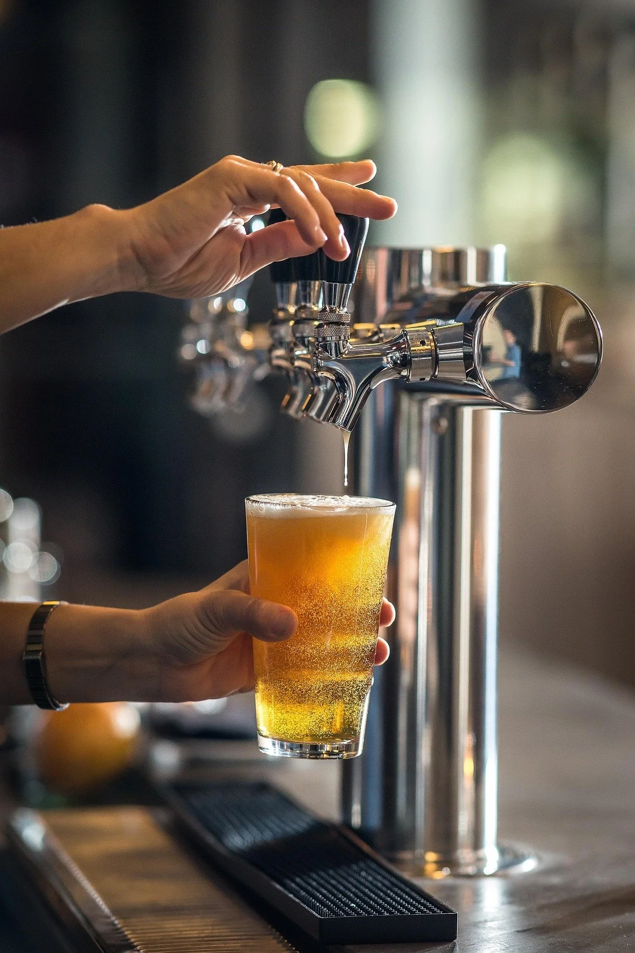 Person pouring beer from a tap into a glass in a bar or brewery setting.