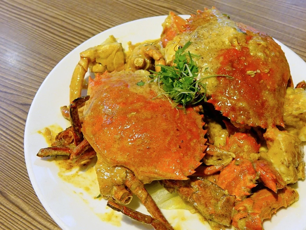 Cooked crabs topped with sauce and garnished with greens on a white plate.