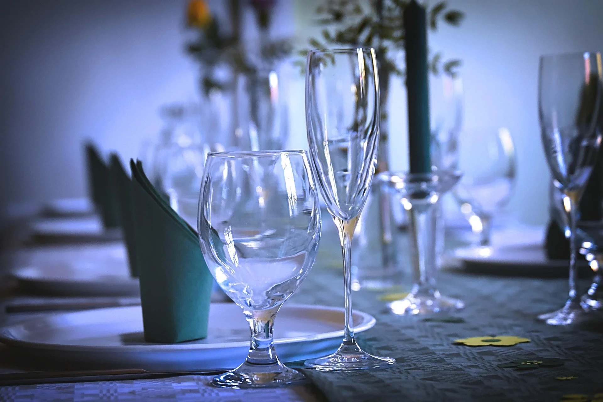 Elegant table setting with wine and champagne glasses, teal napkins, a decorative tablecloth, and candles in the background.