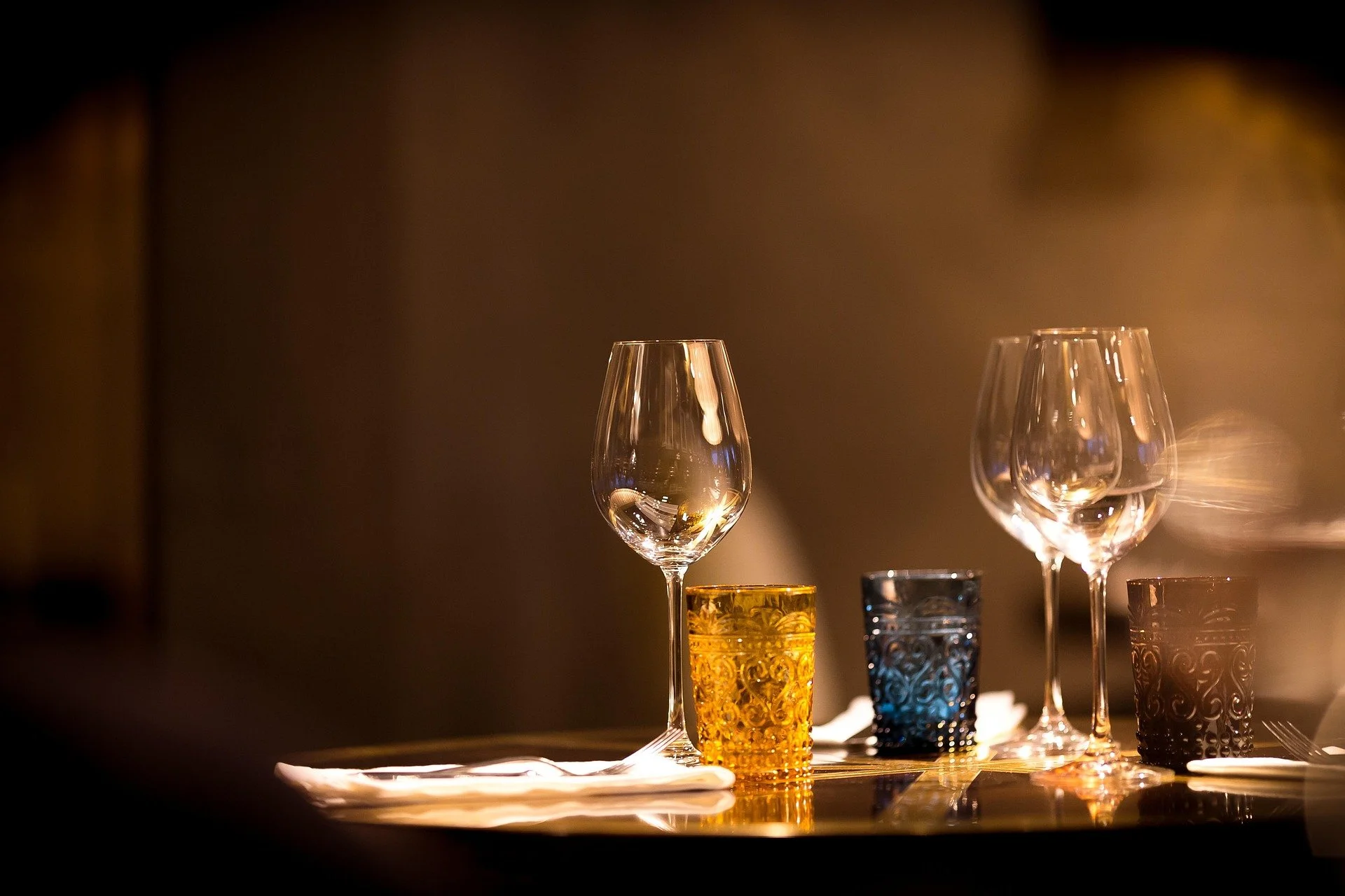 Empty wine glasses and colorful drinking glasses on a table with a blurred background.
