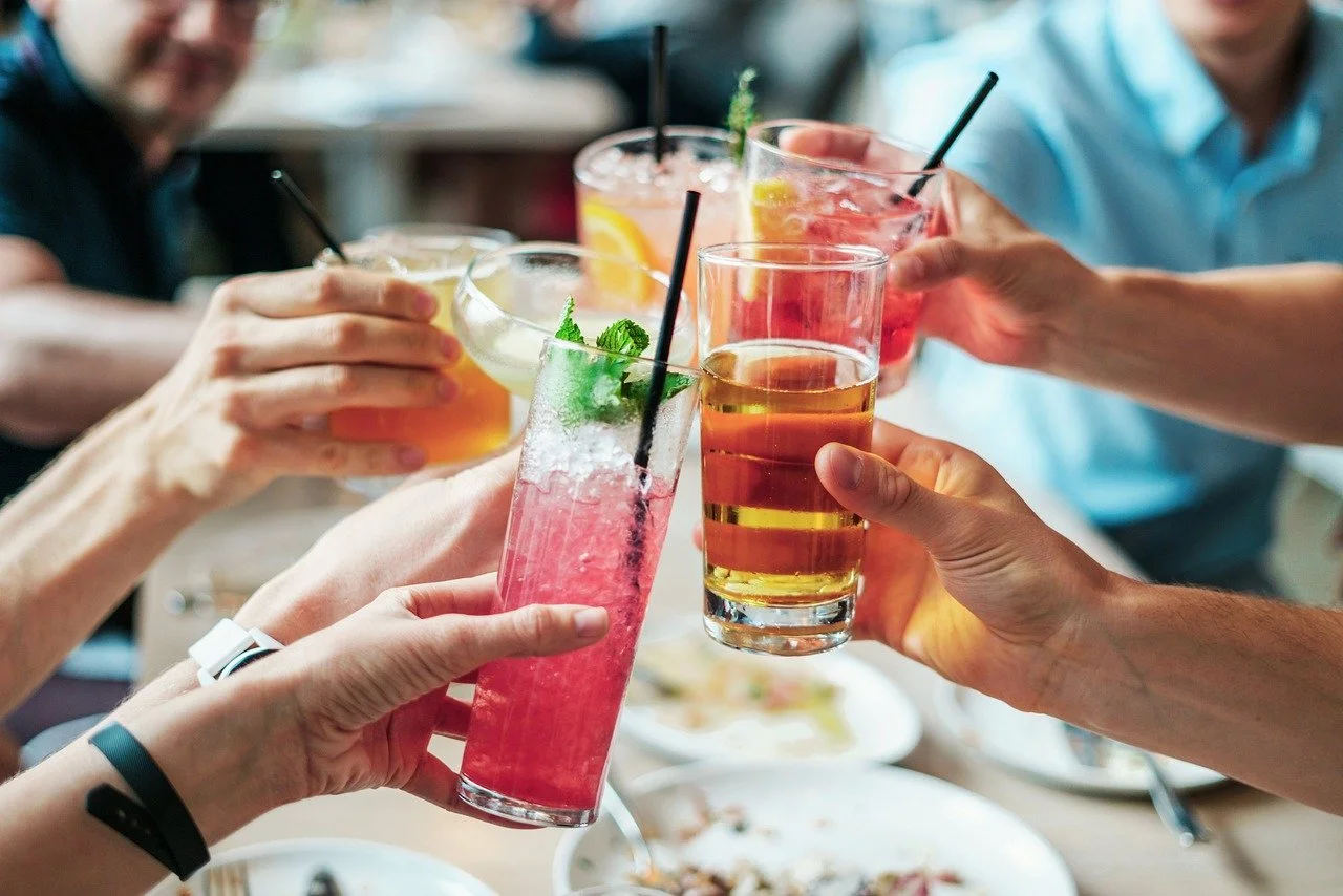 Group of people toasting with colorful cocktails at a dining table.