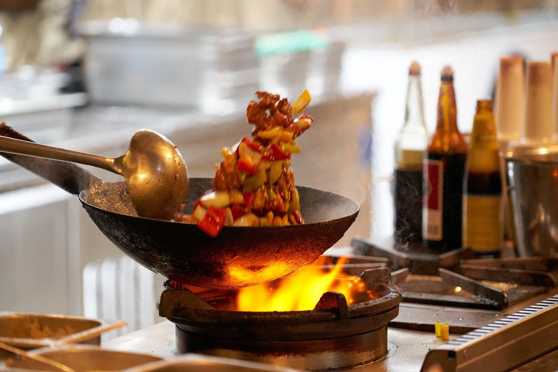 A wok on a stove with stir-fried vegetables and possibly meat, being tossed in mid-air.