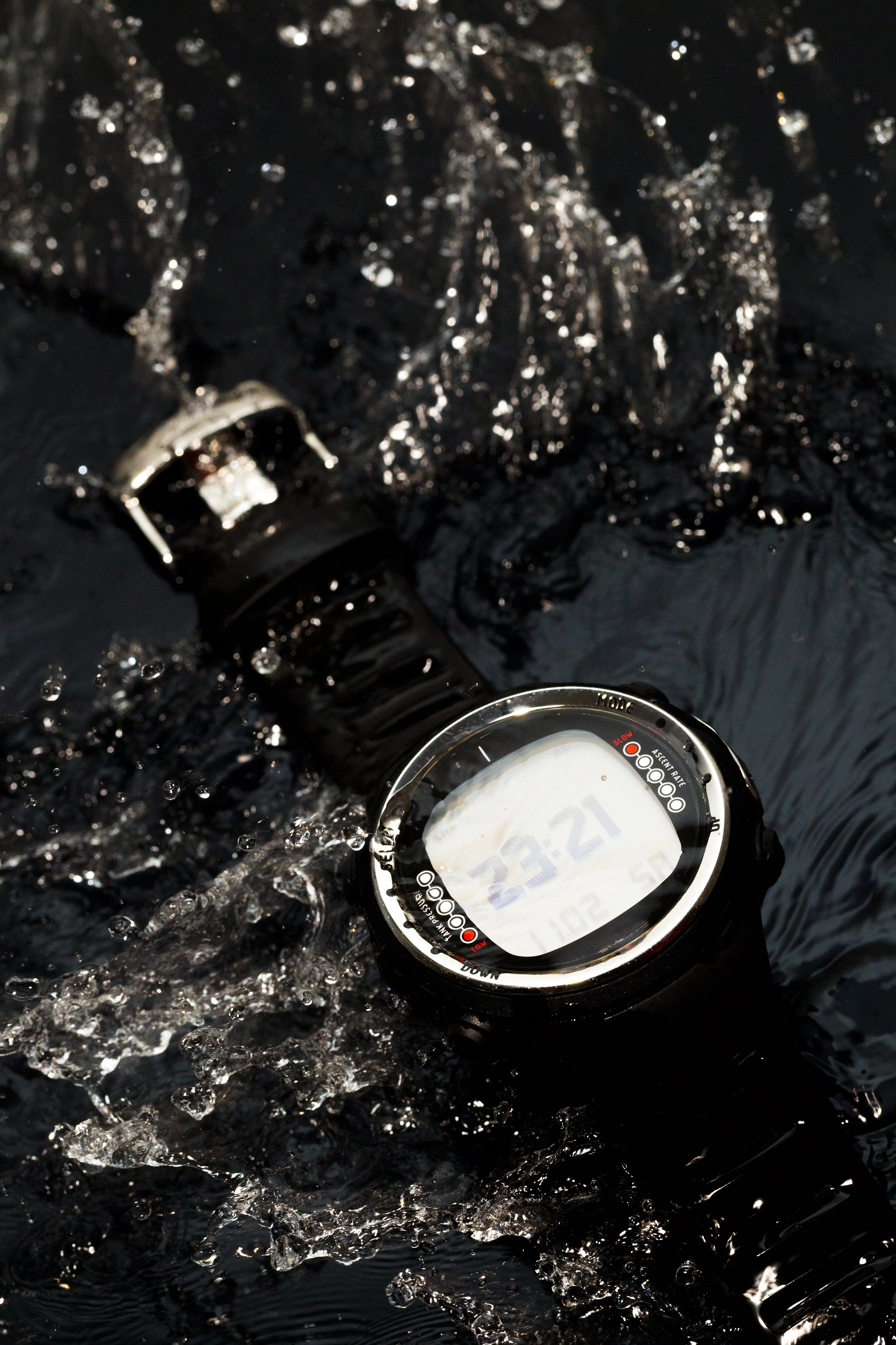 A black digital sports watch submerged in water, with water splashing around it, showing a time of 12:45.