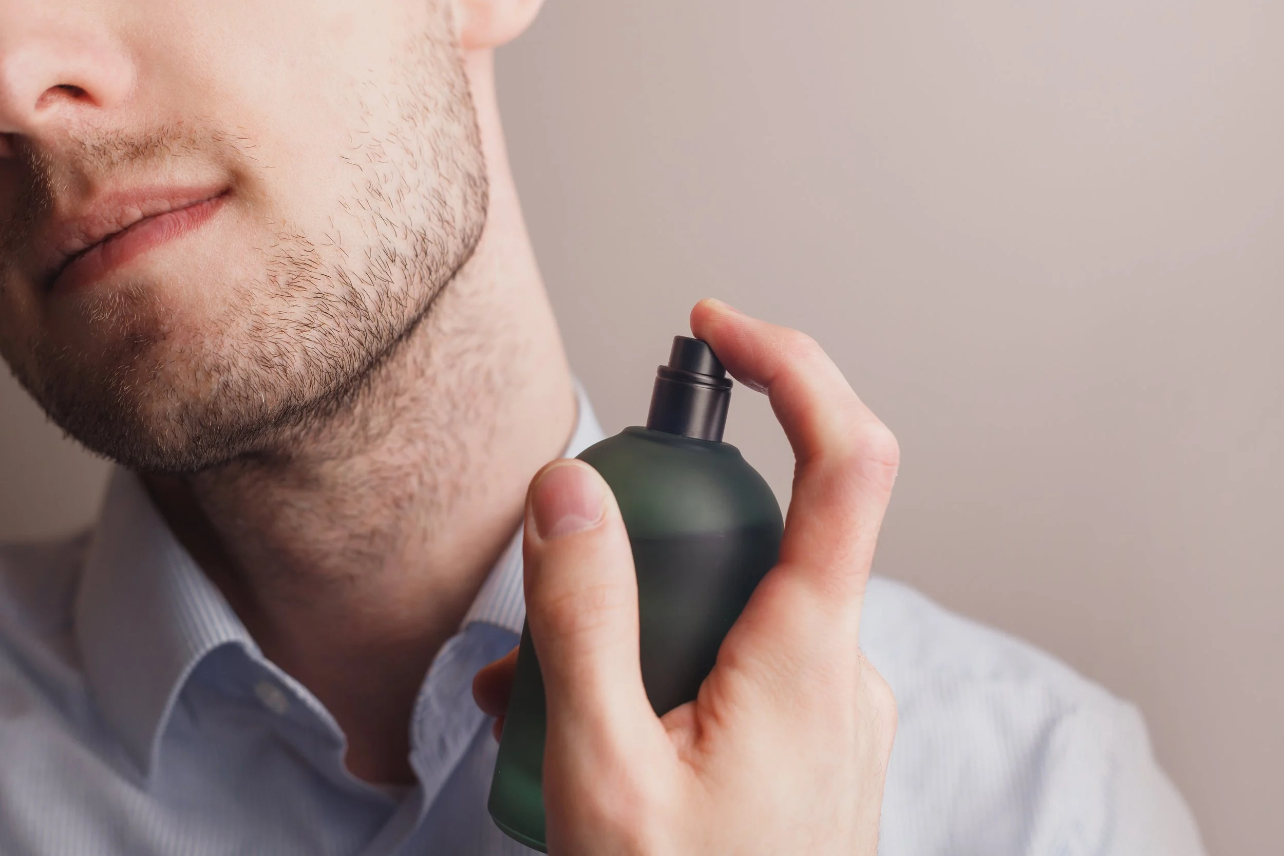 Close-up of a man spraying cologne or perfume on his neck, holding a green bottle