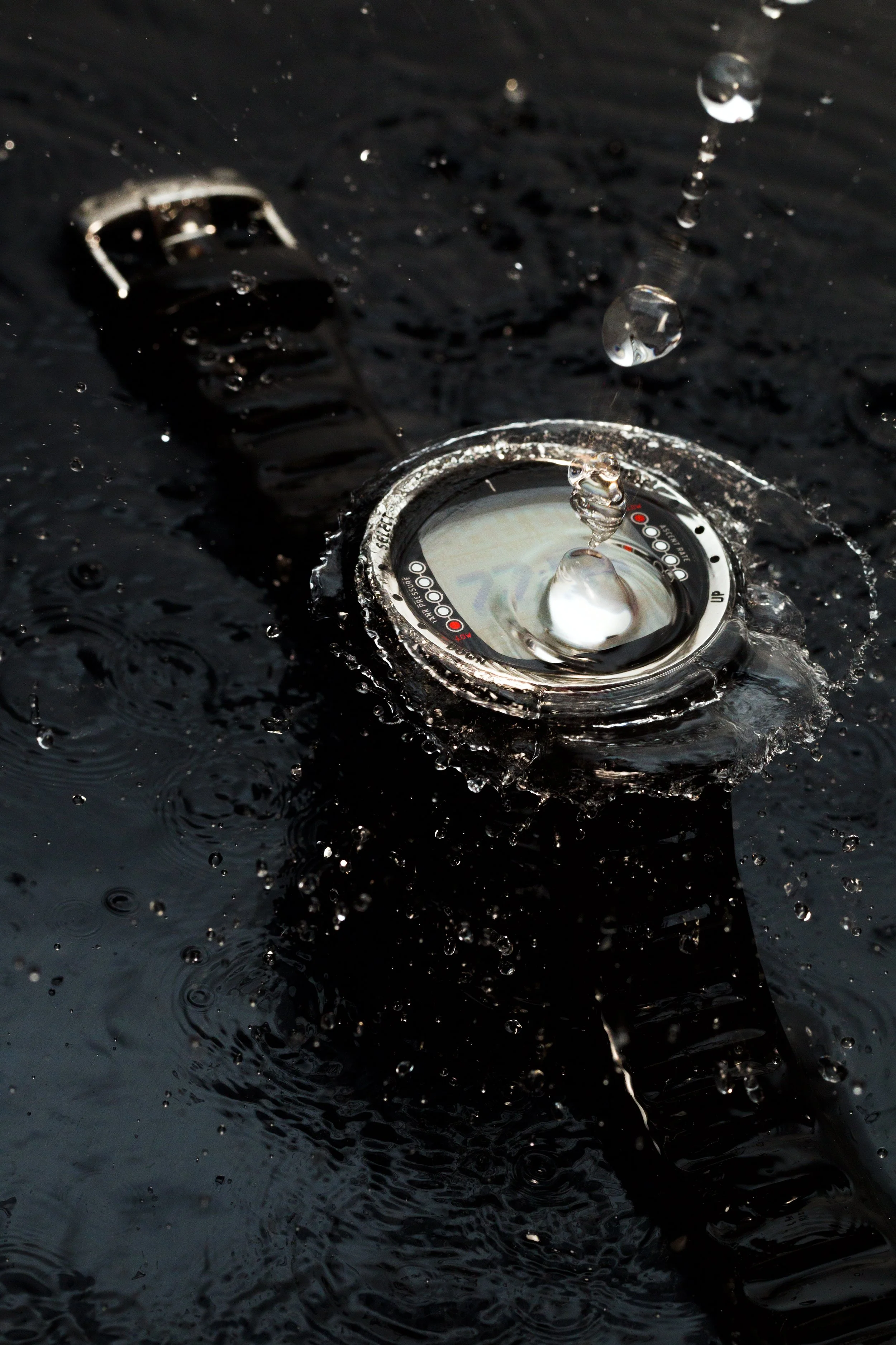 A black wristwatch and a fitness tracker submerged in water with droplets splashing off.