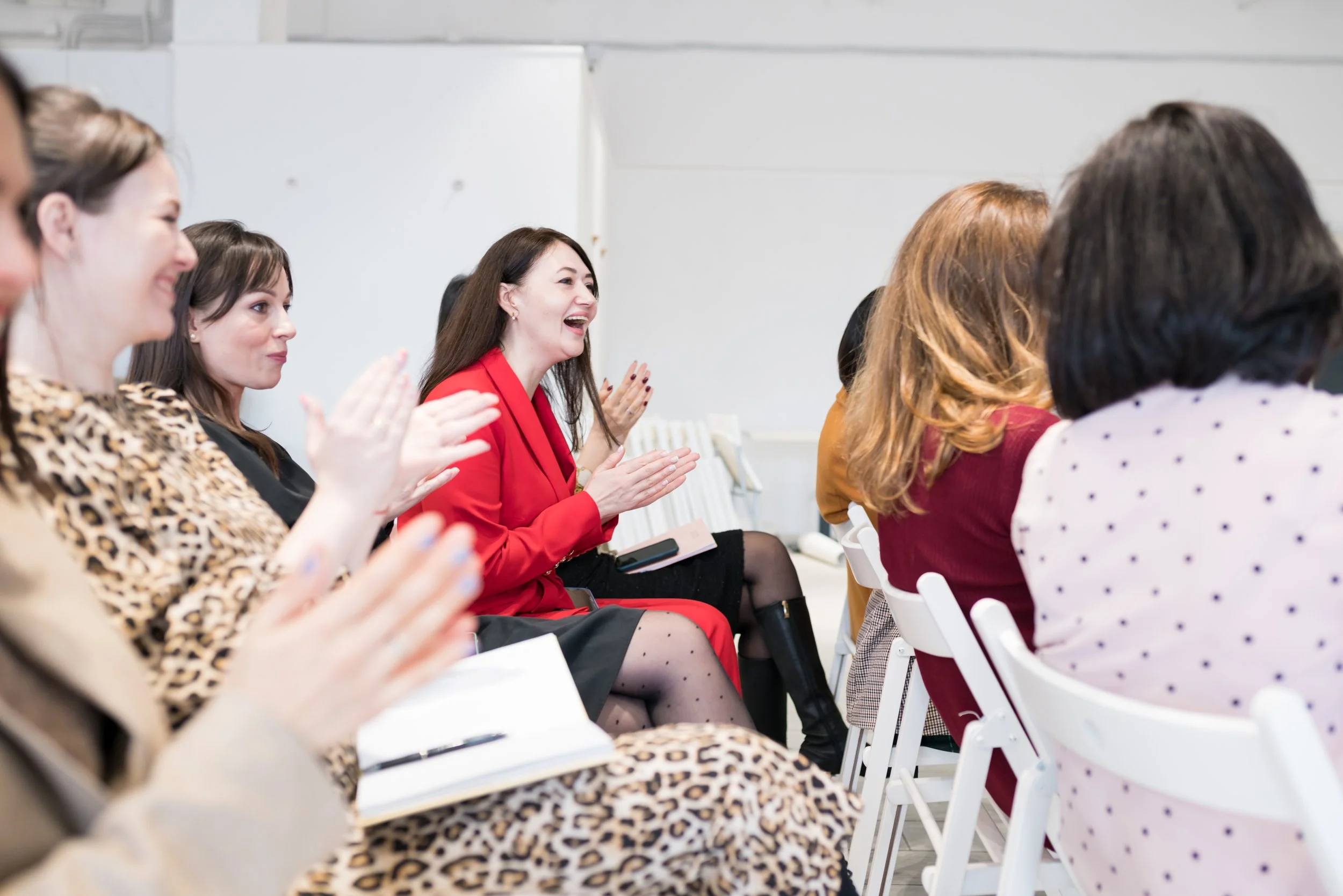Group of women sitting and clapping, some are smiling and laughing during an event or presentation.