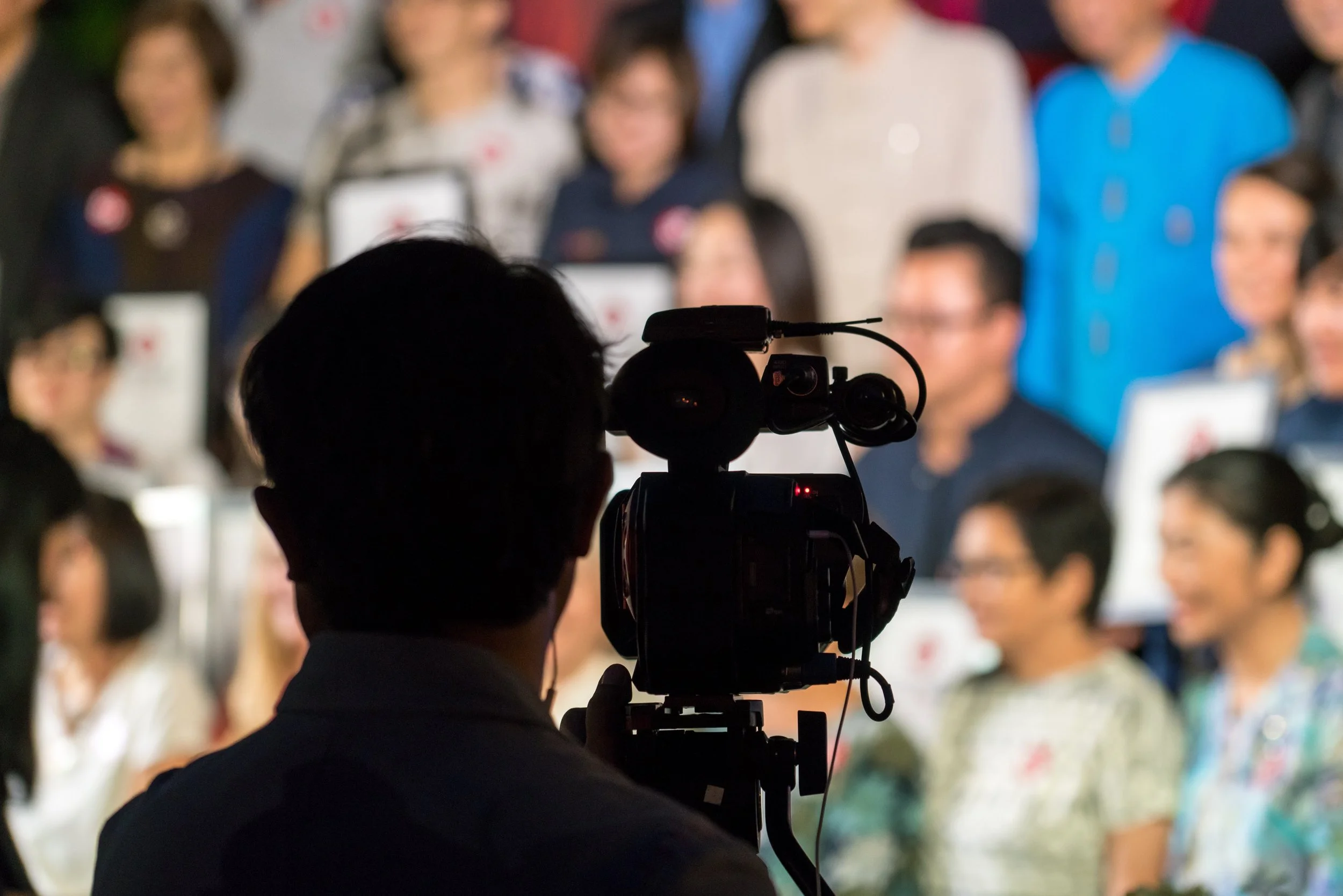 Silhouette of a cameraman filming or photographing a group of smiling people in a formal setting.