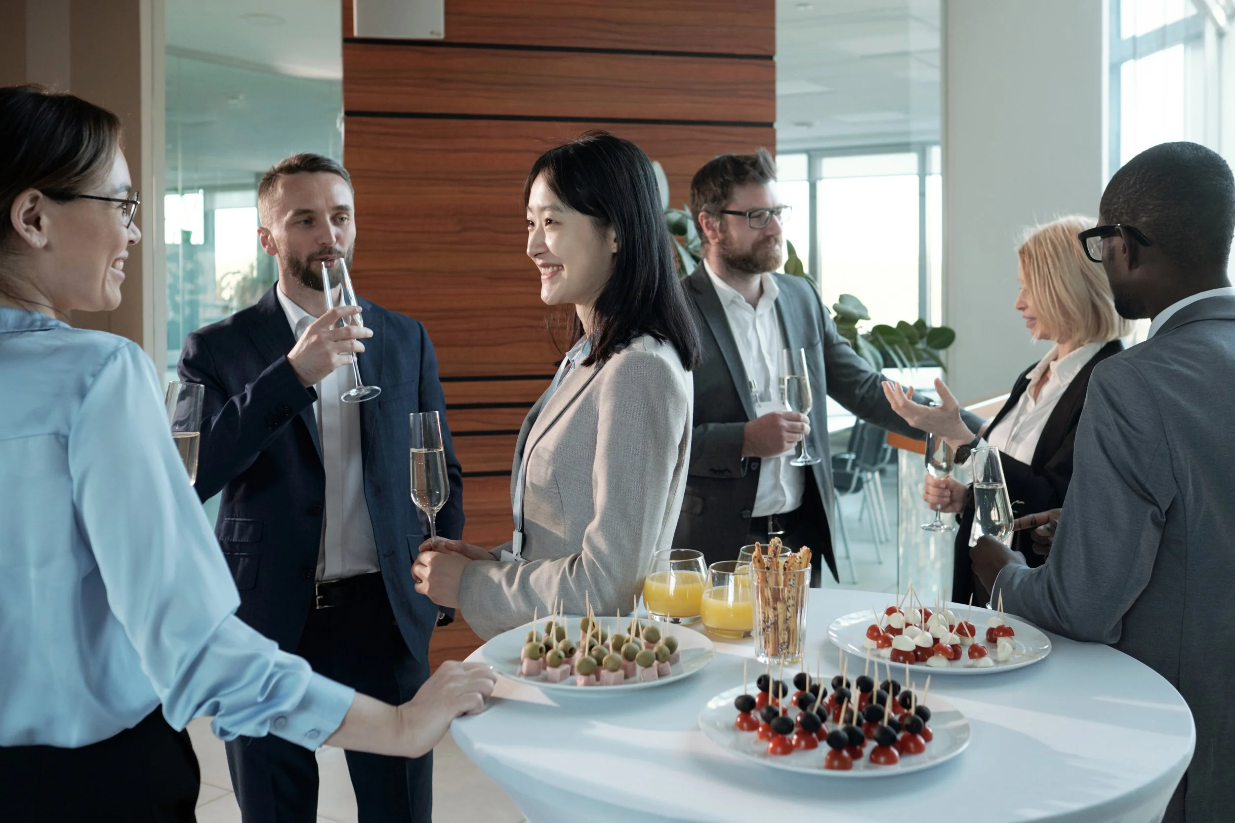 Business professionals socializing and enjoying appetizers and drinks at a networking event or conference in a modern office space.