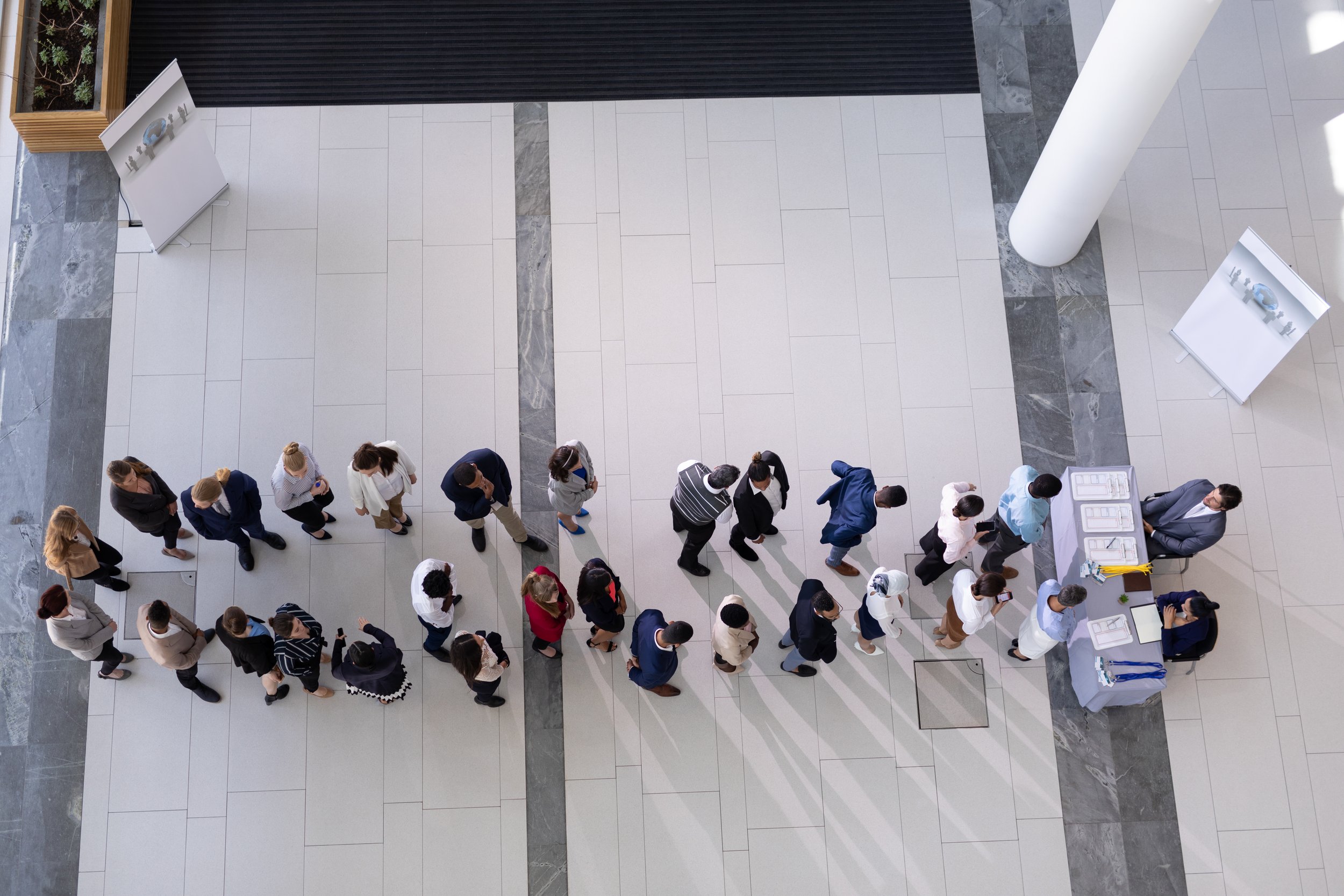 People standing in line at a registration or check-in desk inside a modern building.