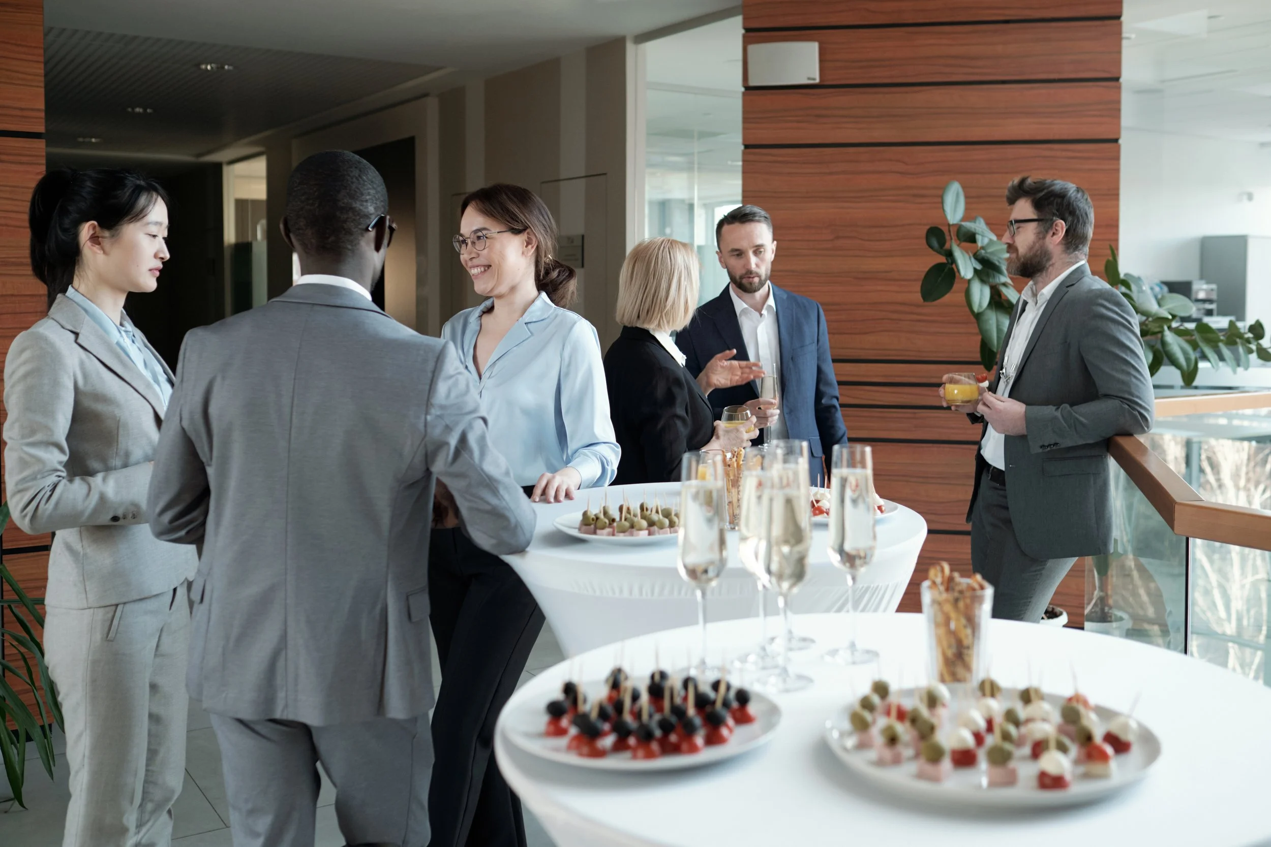 Business professionals socializing at a networking event with a table of appetizers and drinks.
