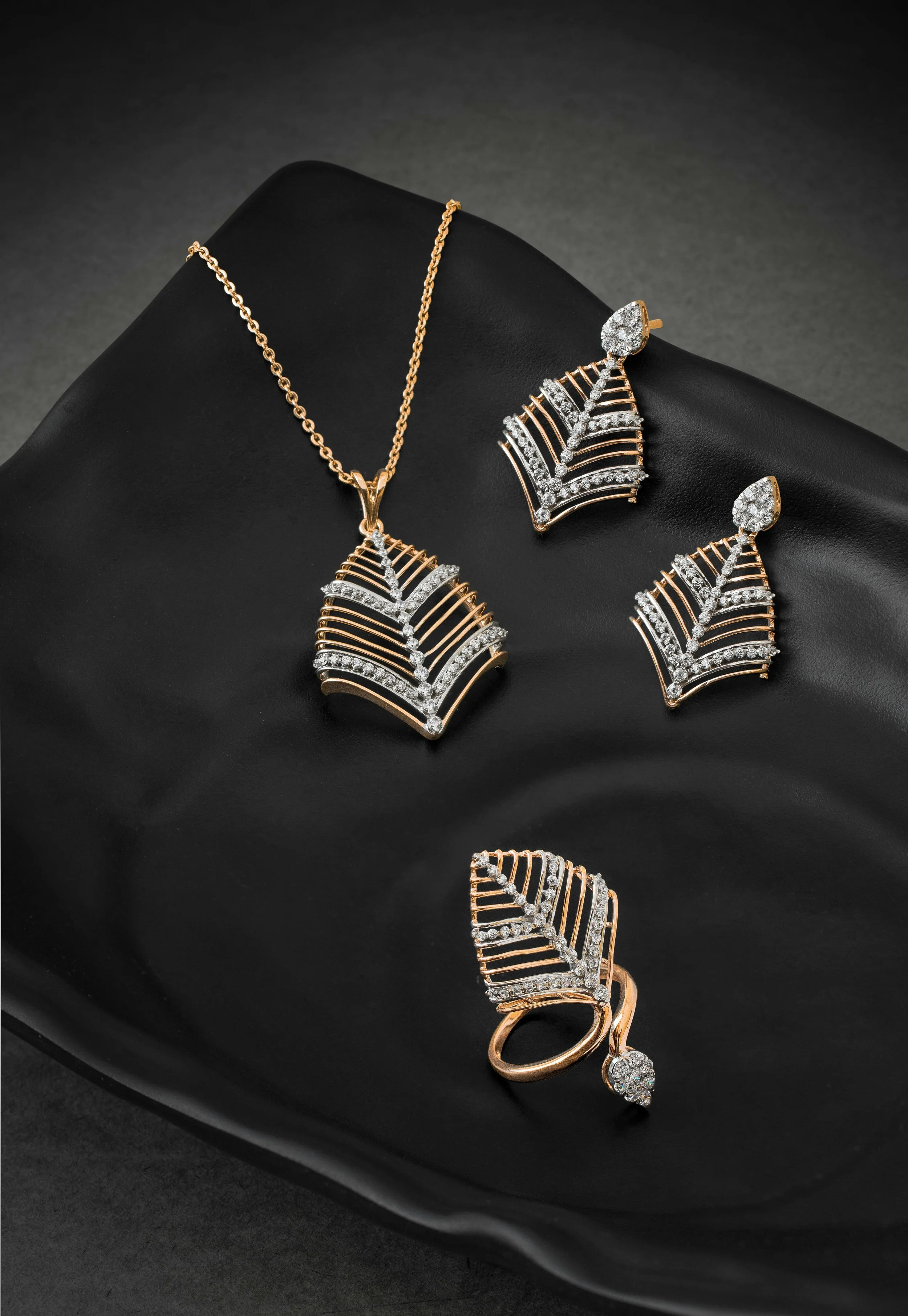 Gold and silver jewelry set including a necklace, earrings, a ring, and a bracelet, all with a fan-like design decorated with diamonds, displayed on a black surface.