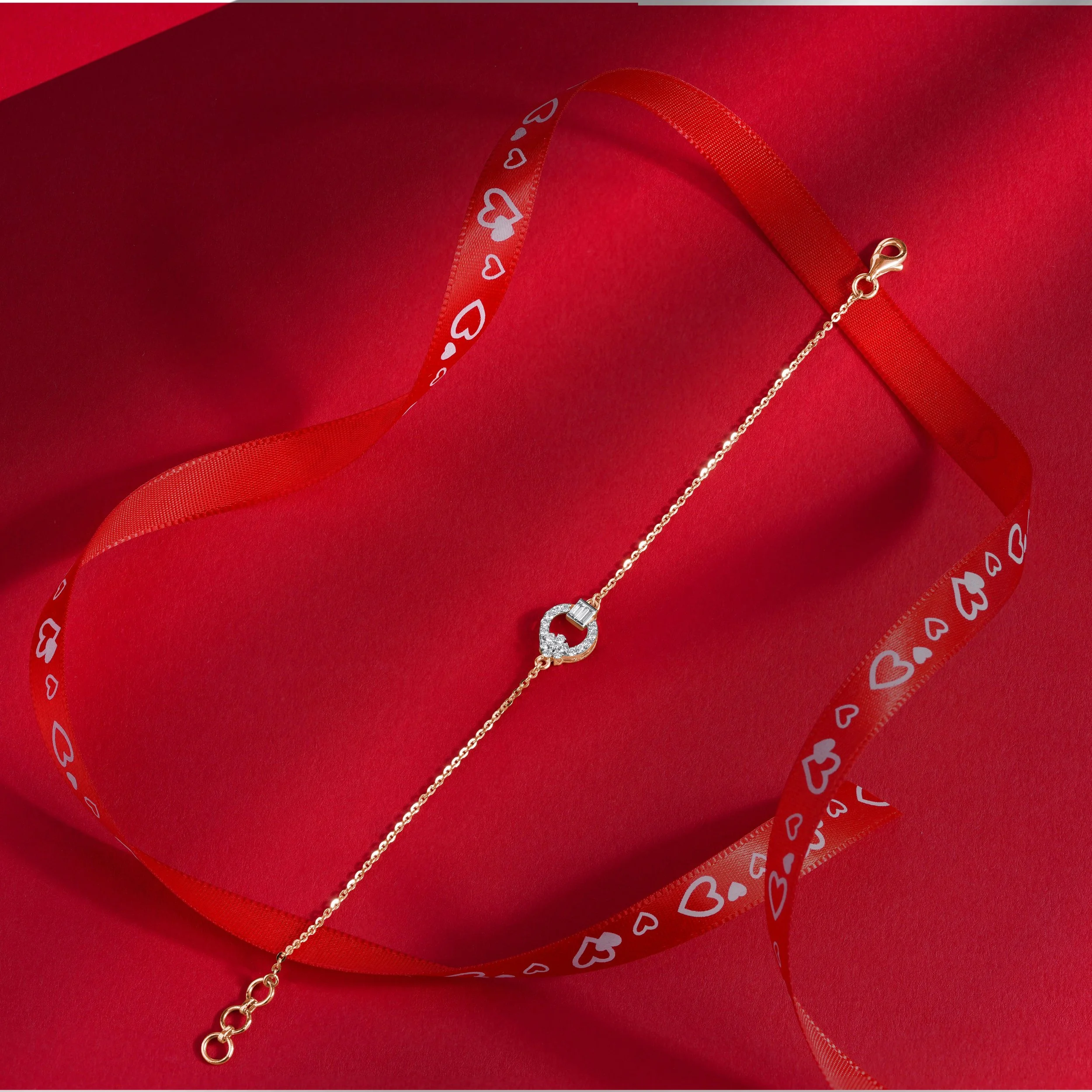 Gold bracelet with a circular charm adorned with small diamonds, lying on a red background with a red ribbon decorated with white hearts.