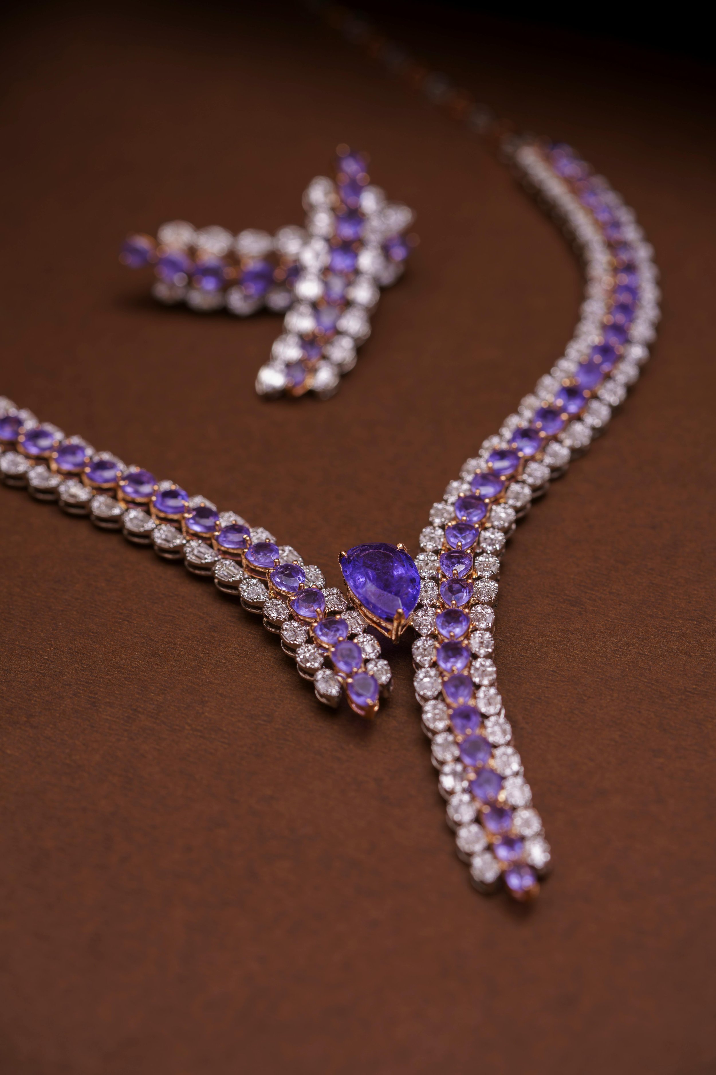 A purple gemstone necklace, earrings, and ring set laid out on a brown surface.