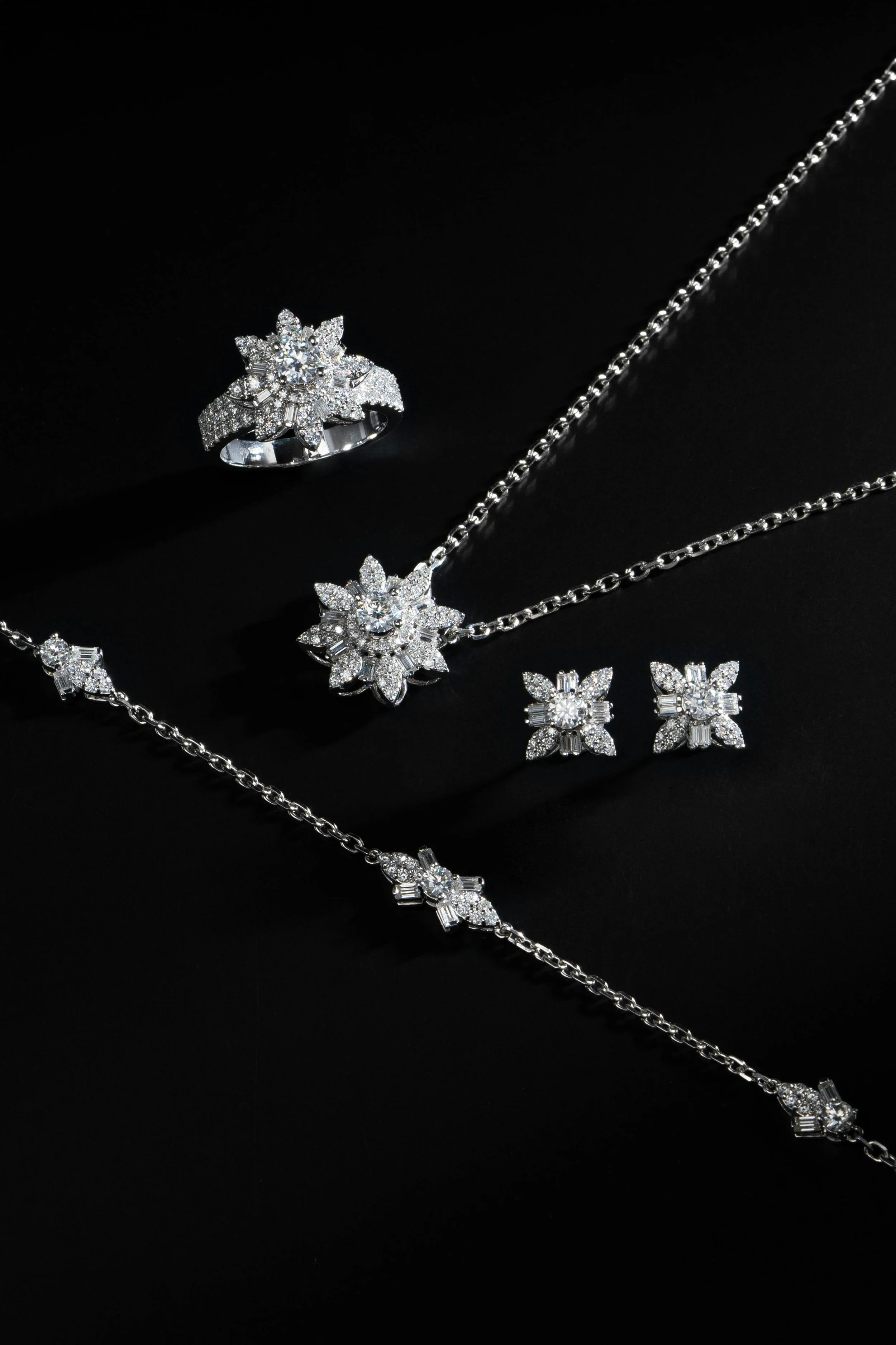 Elegant diamond jewelry set including a ring, necklace, earrings, and a bracelet displayed on a black background.