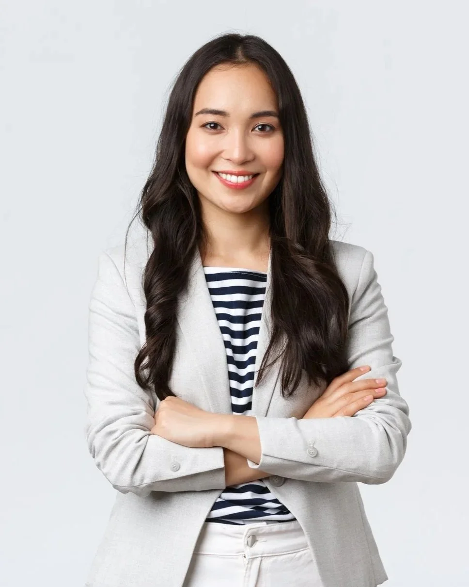 A young woman with long wavy dark hair, smiling, wearing a light-colored blazer over a navy and white striped shirt, with her arms crossed, against a plain white background.