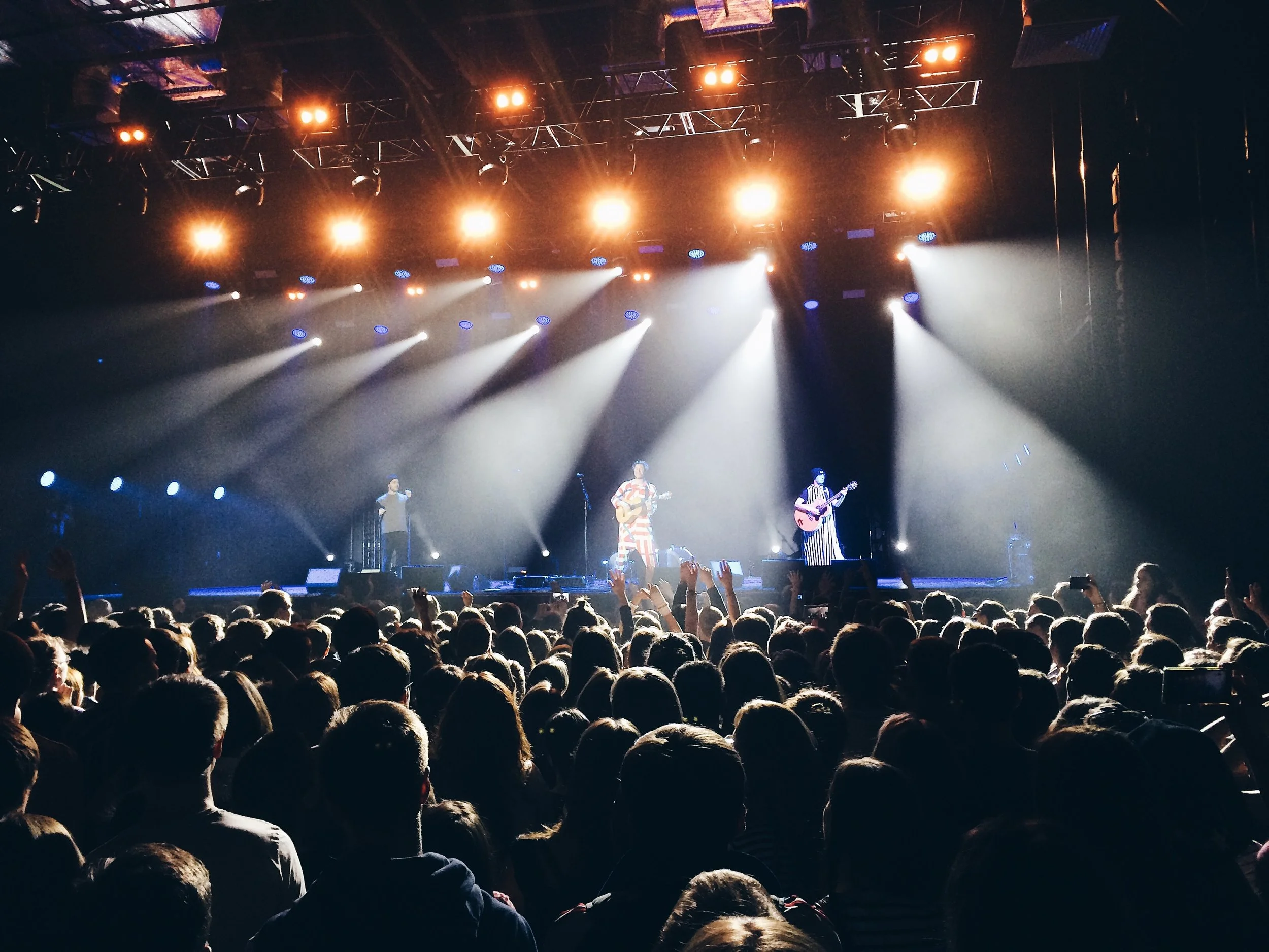 A concert stage with bright lights and performers, including a guitarist and a singer, in front of a large audience.