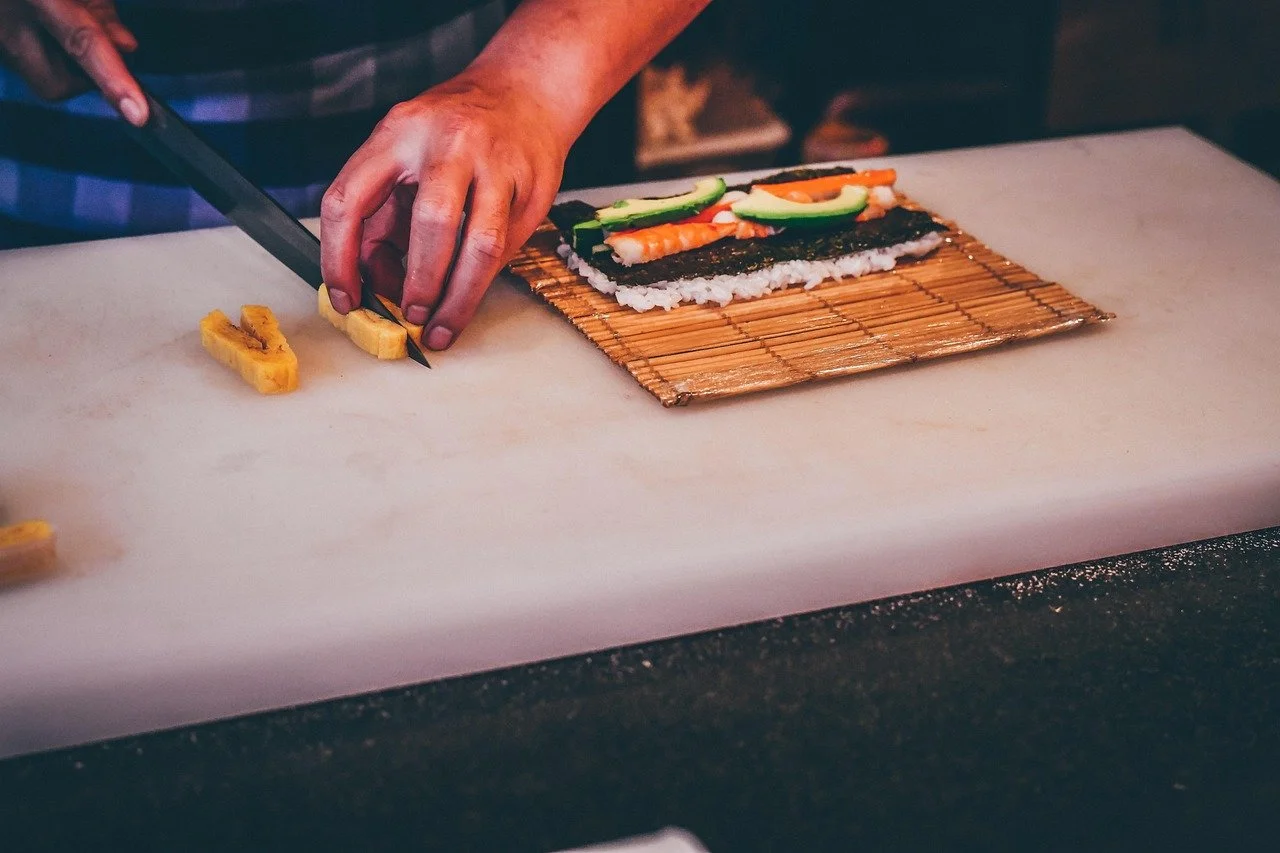Person preparing sushi with seaweed, rice, avocado, and shrimp on bamboo mat.