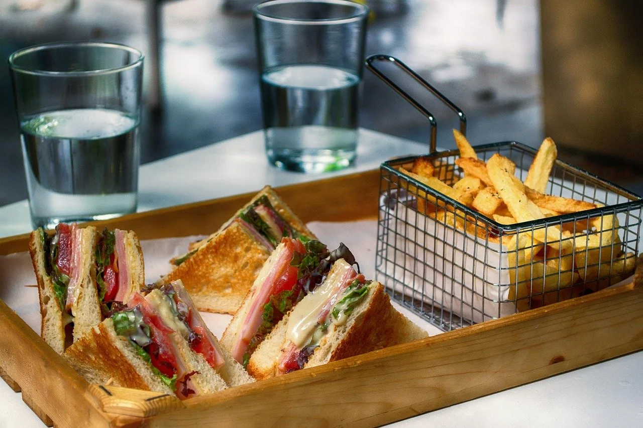 Club sandwiches with lettuce, tomato, ham, and cheese, served with French fries and two glasses of water.