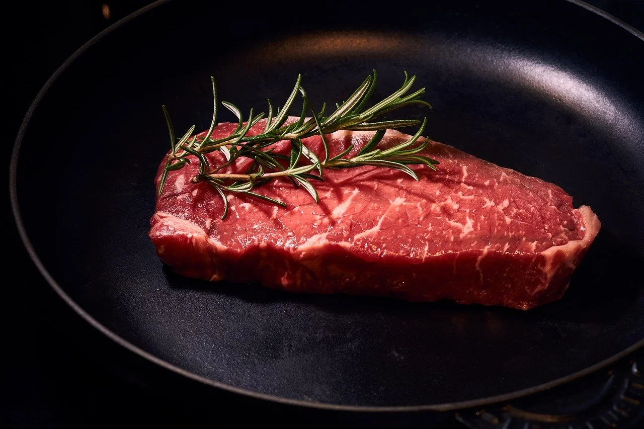 Raw steak with a sprig of rosemary in a black frying pan