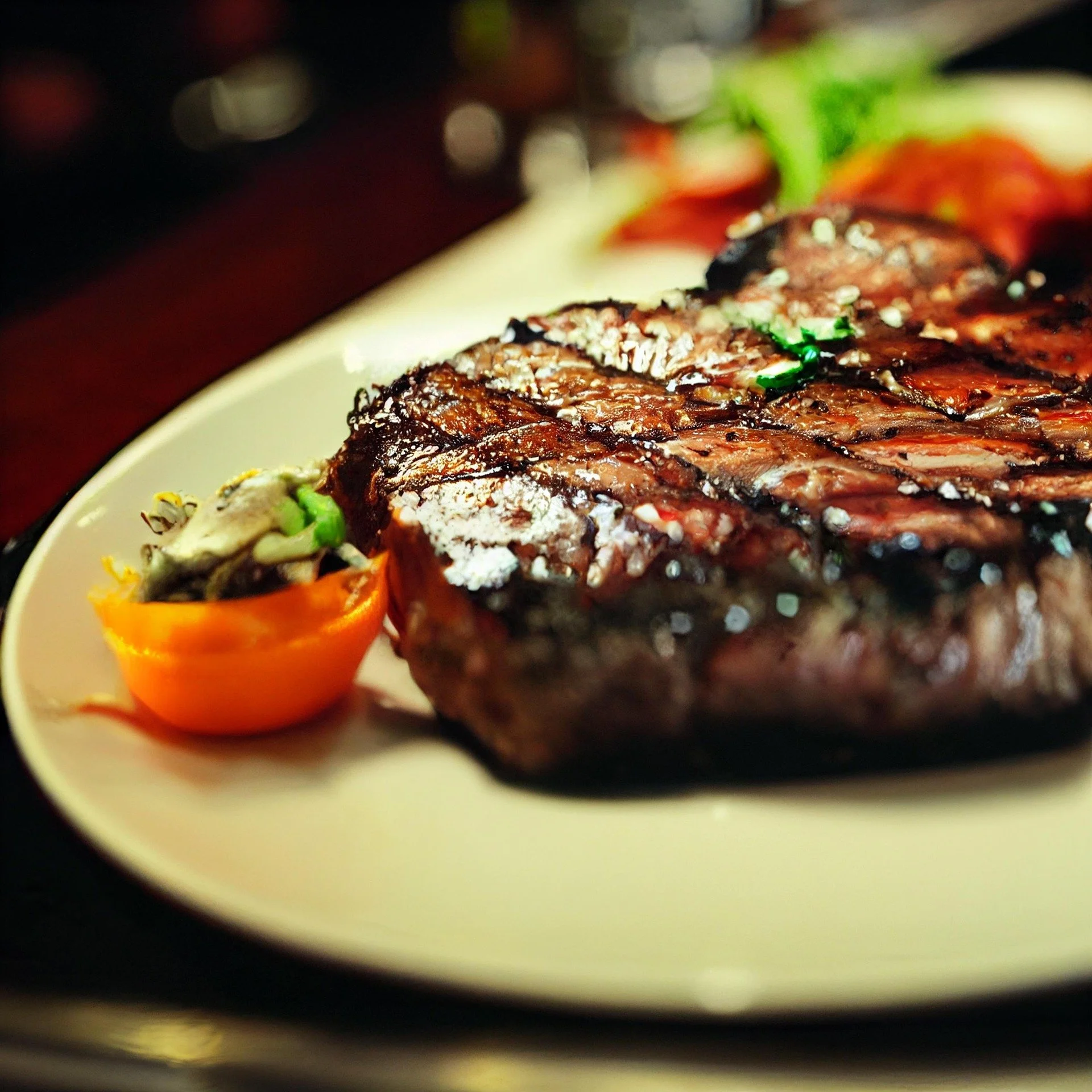 Close-up of a grilled steak with salt, served with a side of vegetables on a white plate.