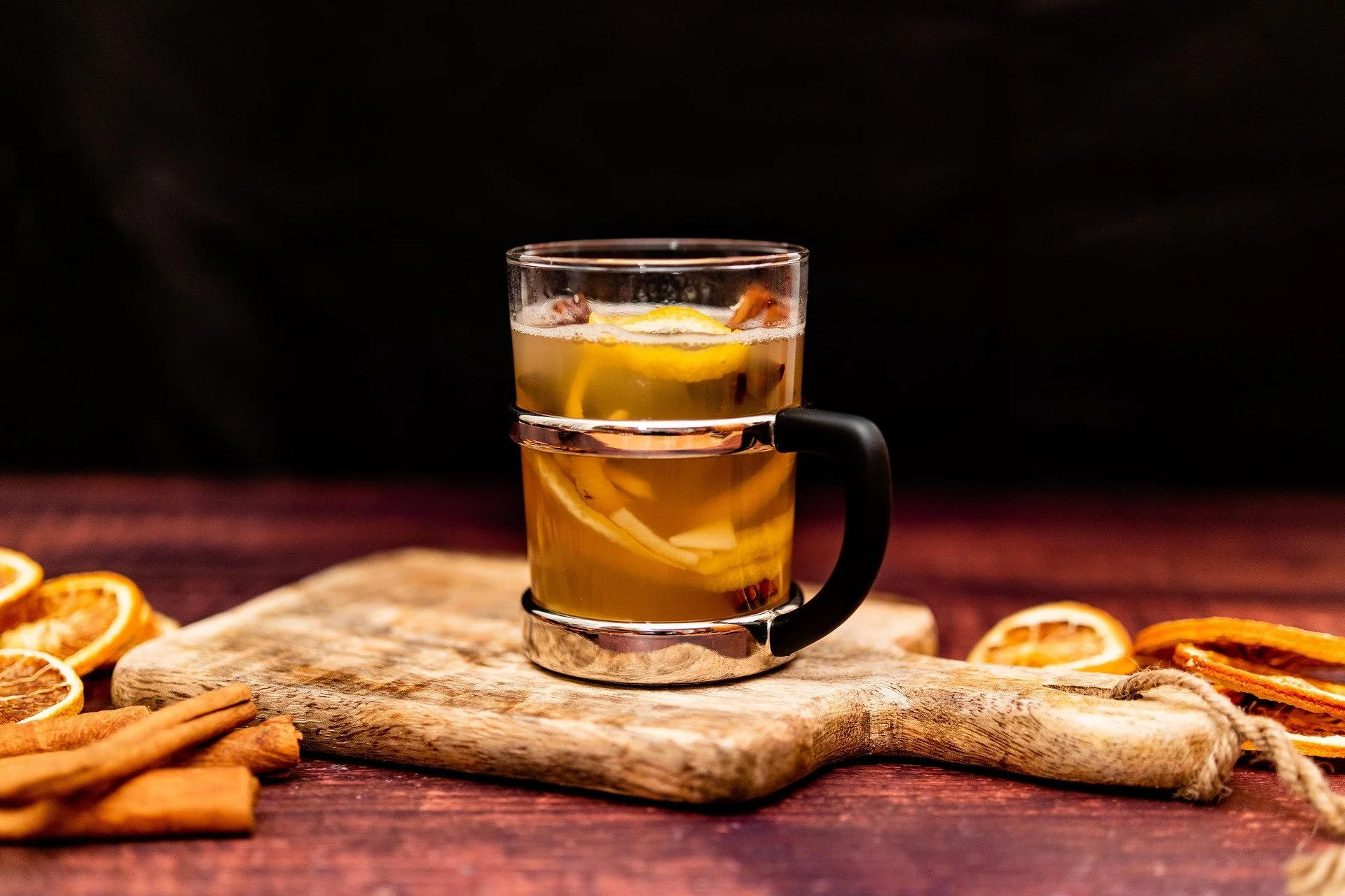 A glass of hot spiced apple cider with lemon slices and cinnamon sticks on a rustic wooden table.