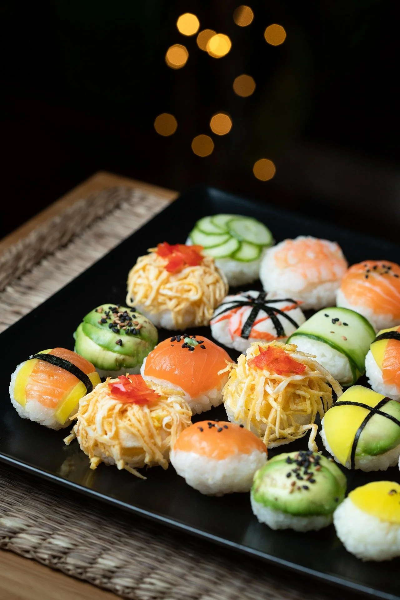 Assorted sushi on a black plate with cucumber, salmon, and shredded egg toppings.