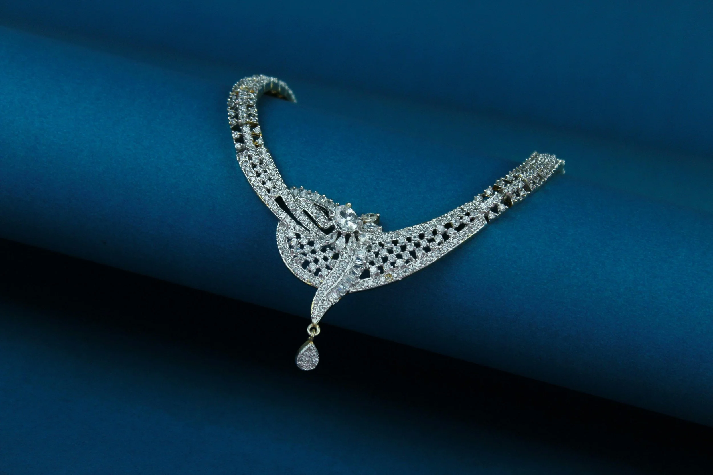 Silver necklace with numerous small diamonds laid on a dark blue fabric background.