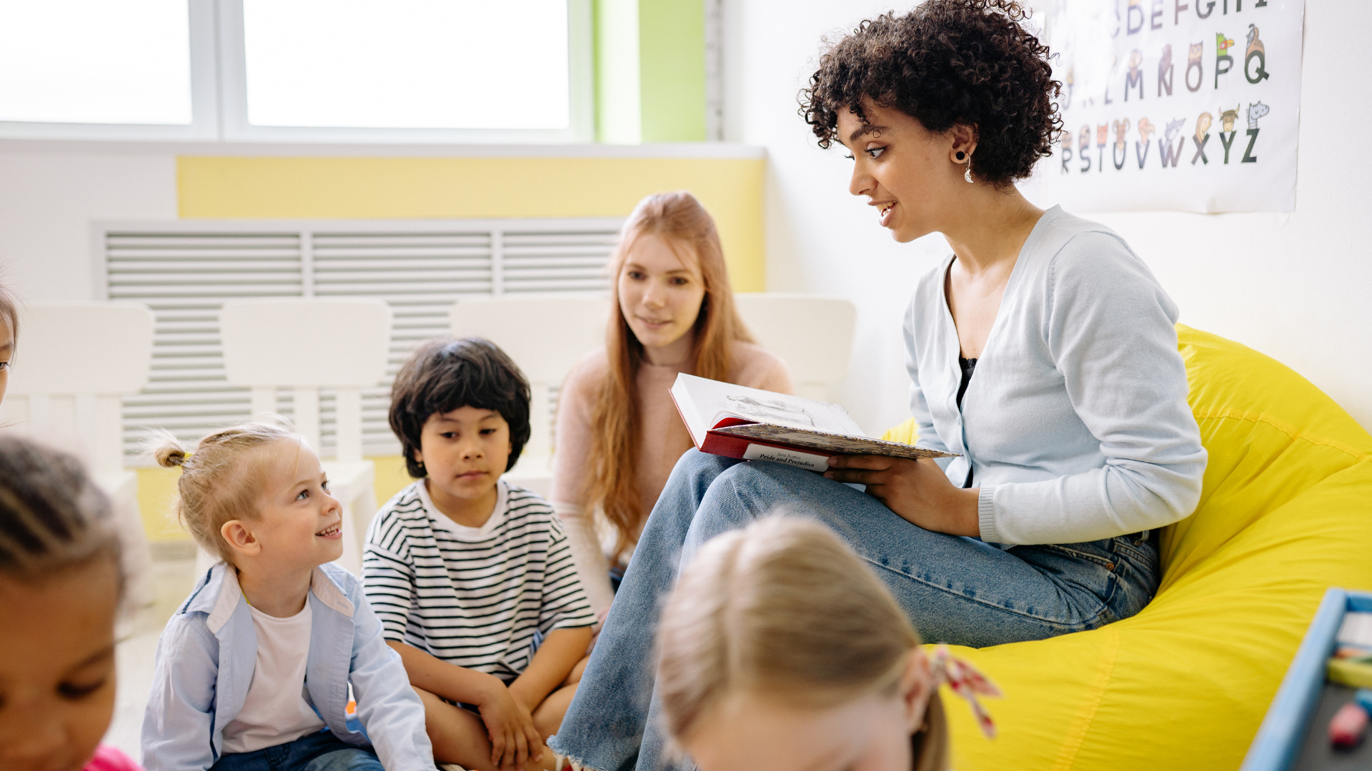 A teacher reading a book to a group of children in a classroom.