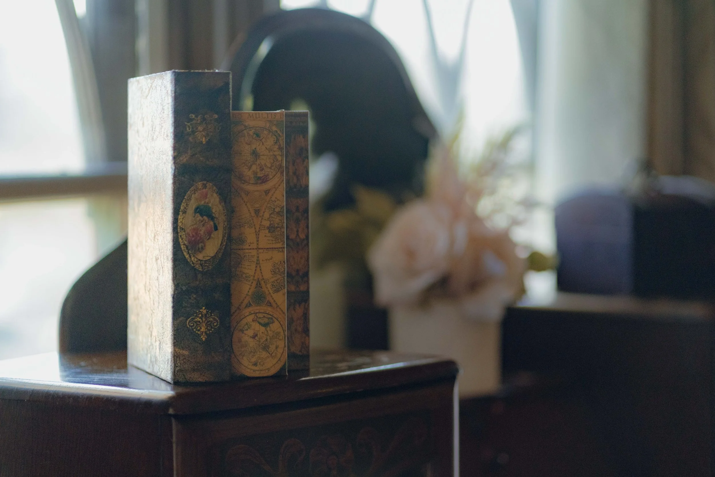 Vintage book on wooden table with decorative cover, blurred background with flowers and soft lighting.