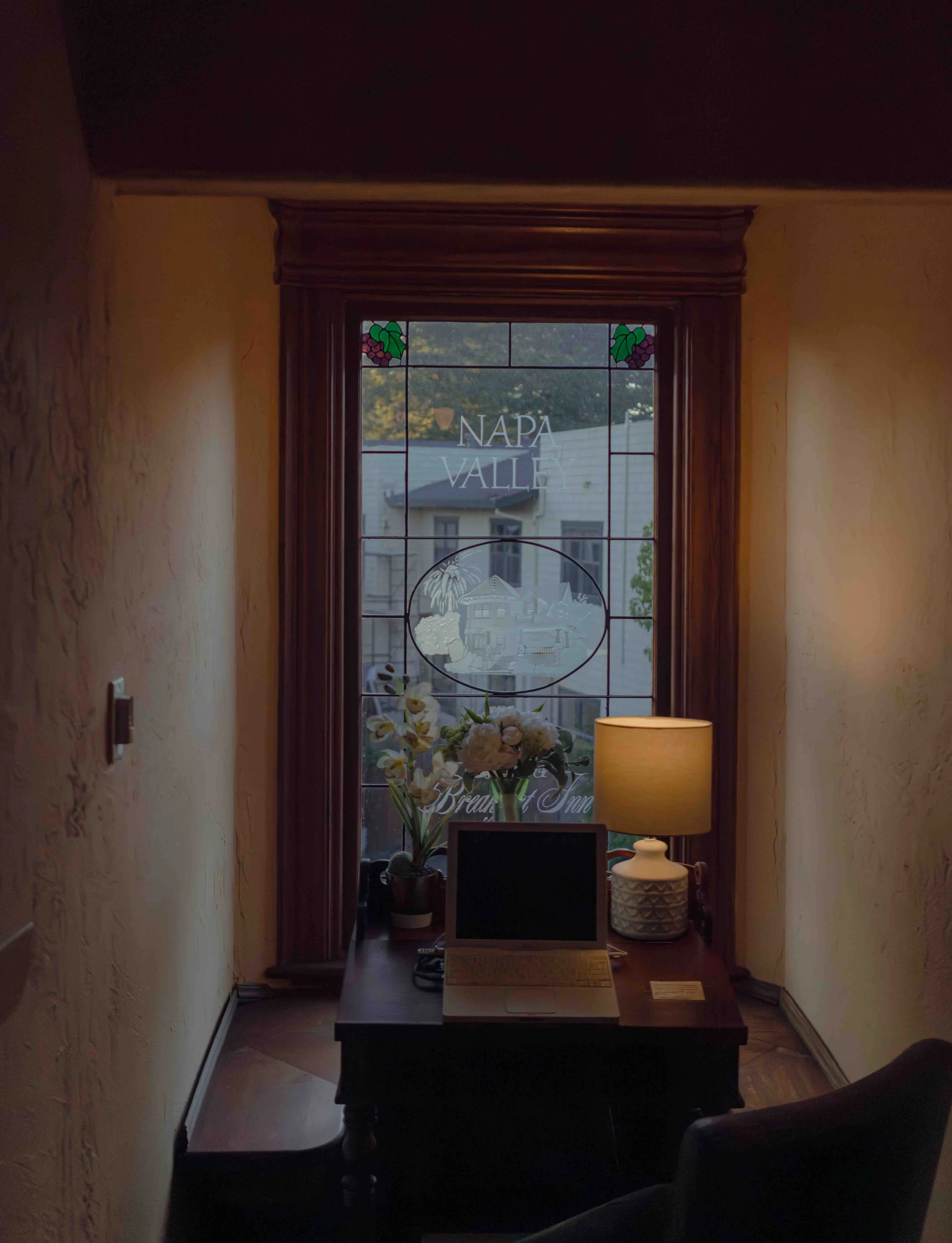 Room with a desk, an open laptop, a lamp, and flowers by a stained glass window with 'Napa Valley' text.