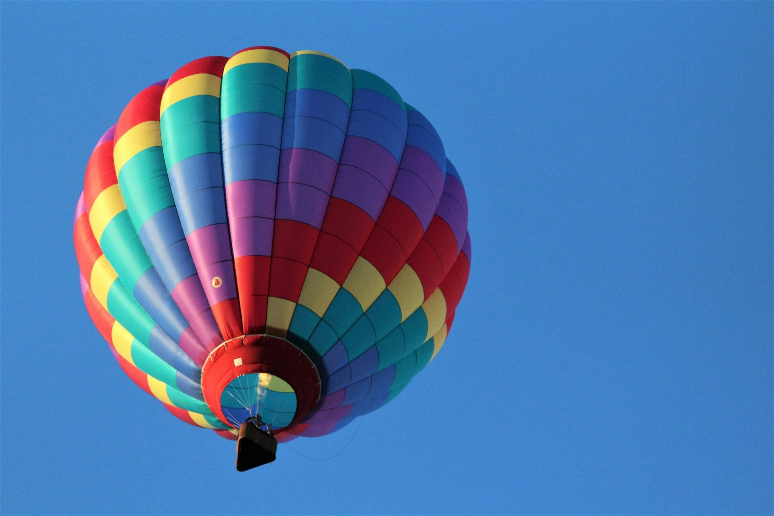 Colorful hot air balloon with rainbow pattern floating in a clear blue sky.