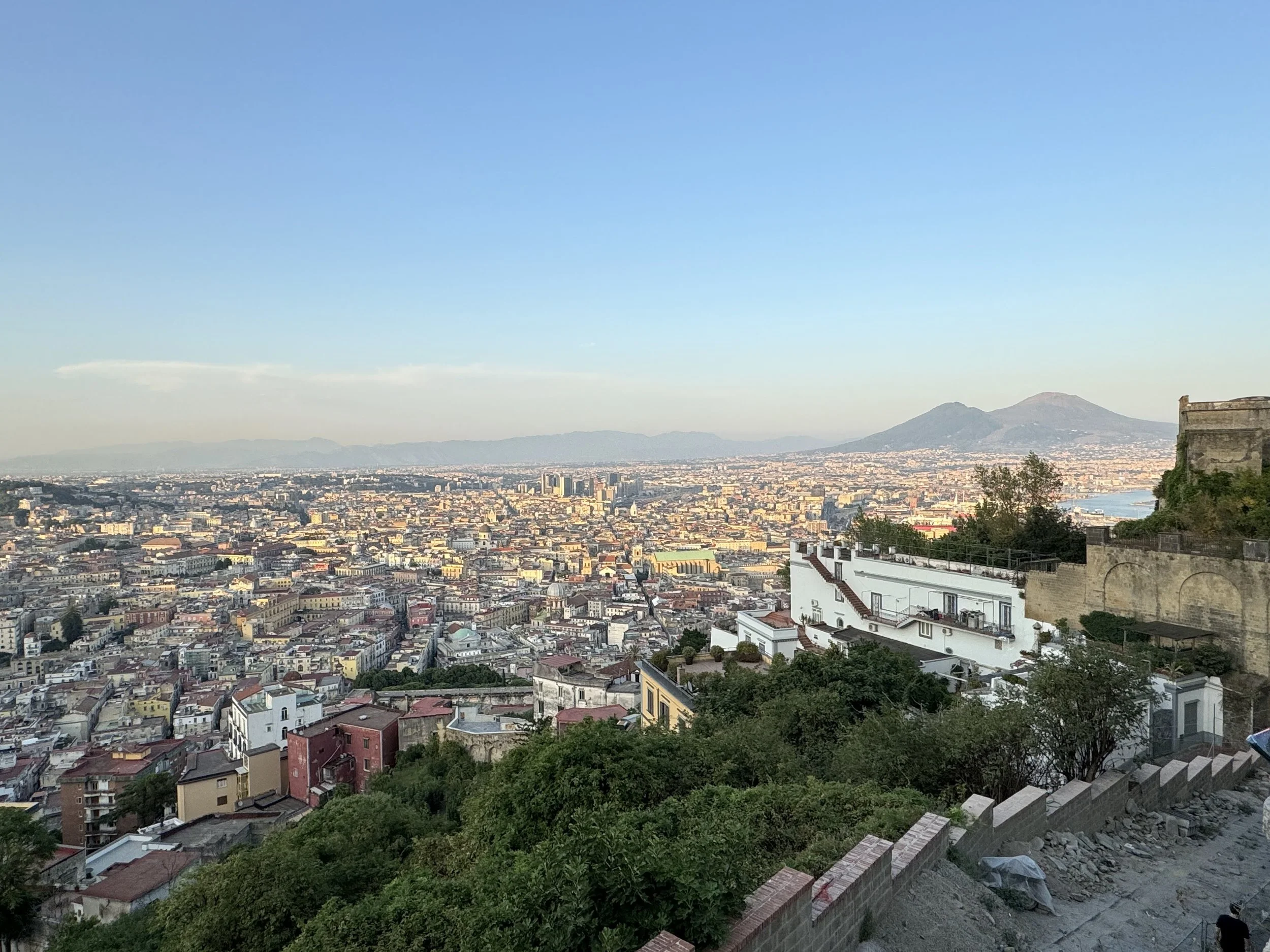 Panorama von Neapel, Italien, mit Stadt und Umgebung, einem Vulkan im Hintergrund und weißen Gebäuden im Vordergrund.