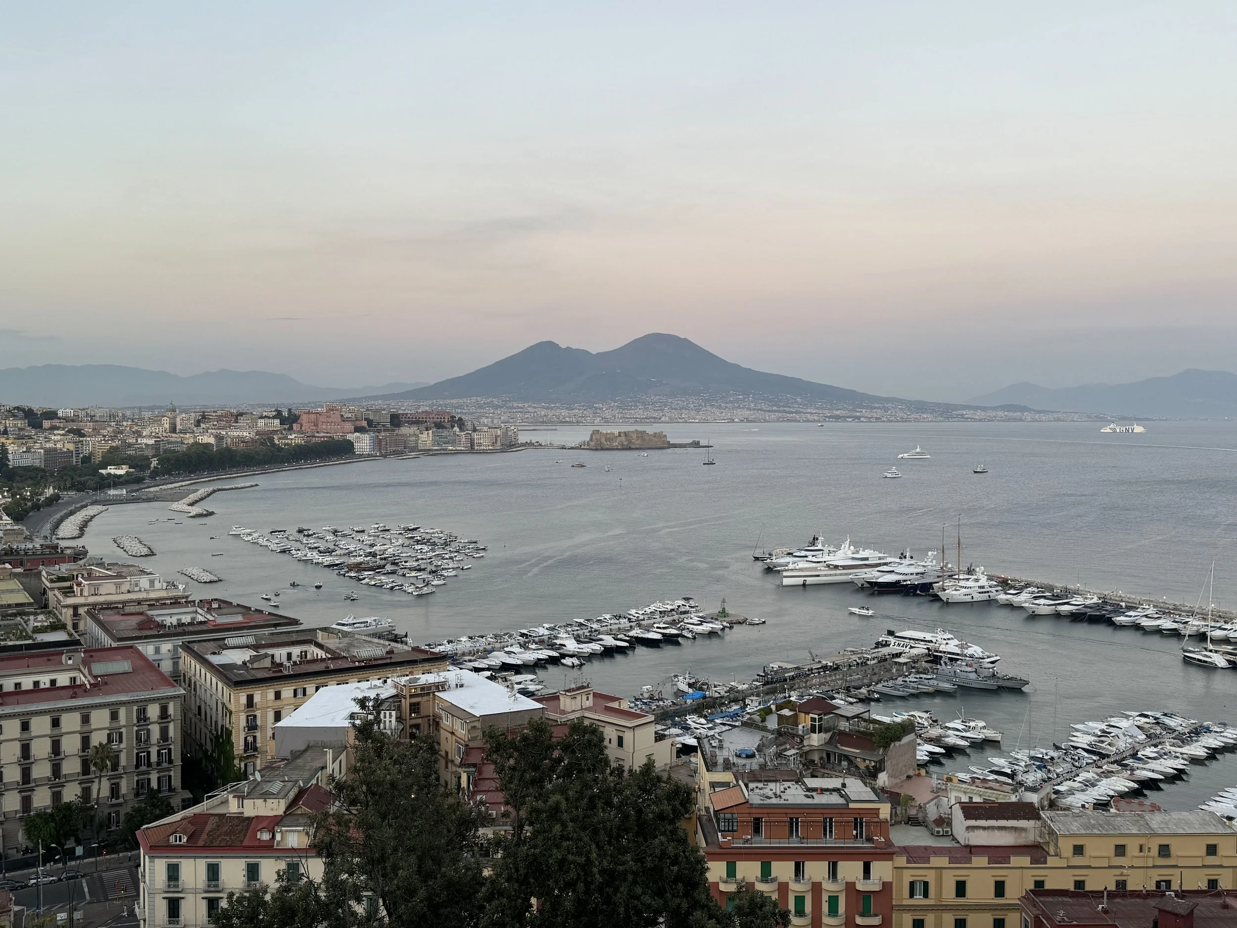Blick auf den Hafen von Neapel mit vielen Yachten und dem Vesuv im Hintergrund bei Sonnenuntergang.