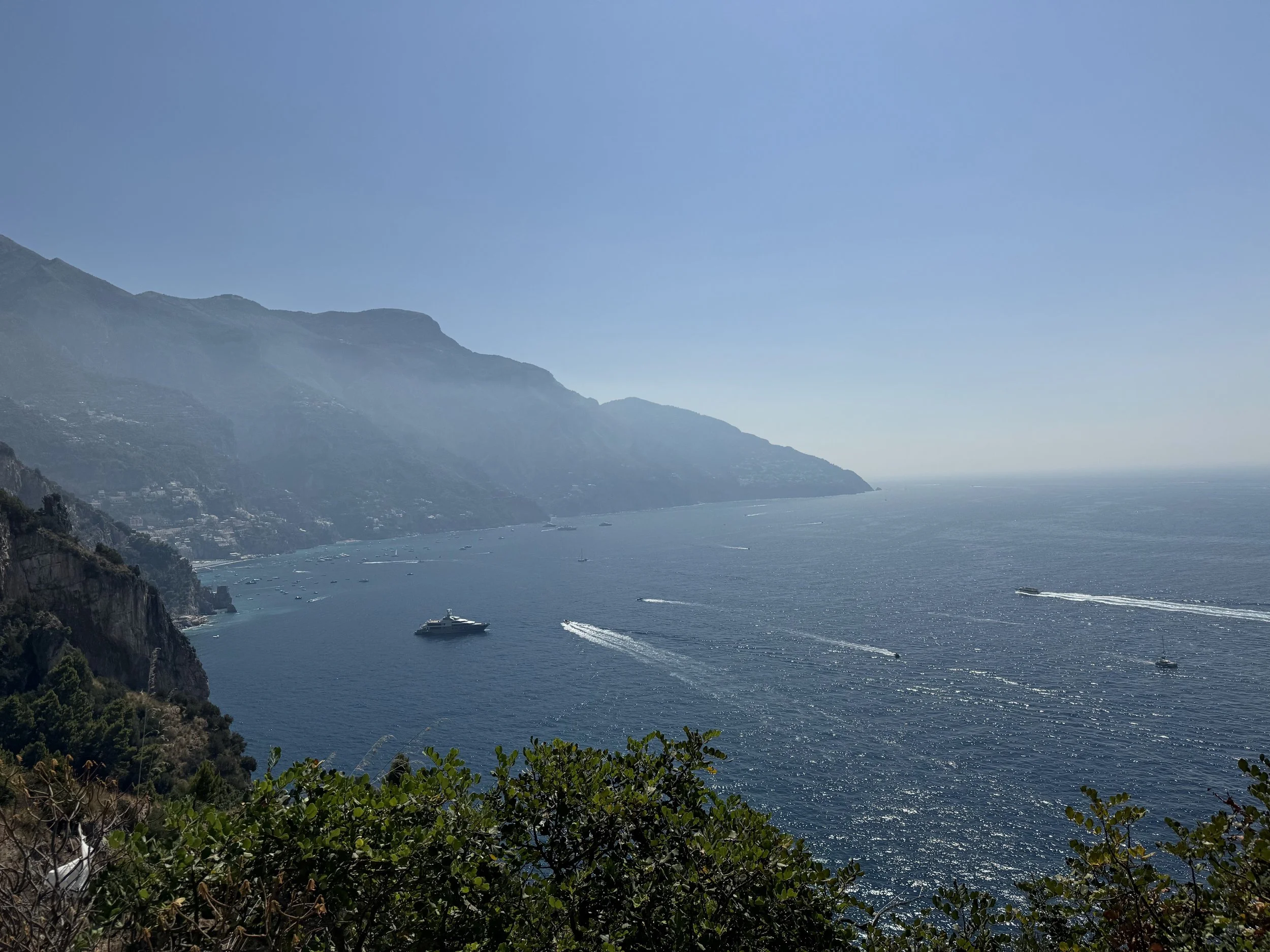 Blick auf das Meer mit mehreren Booten, umgeben von Hügeln und Bergen unter klarem Himmel.