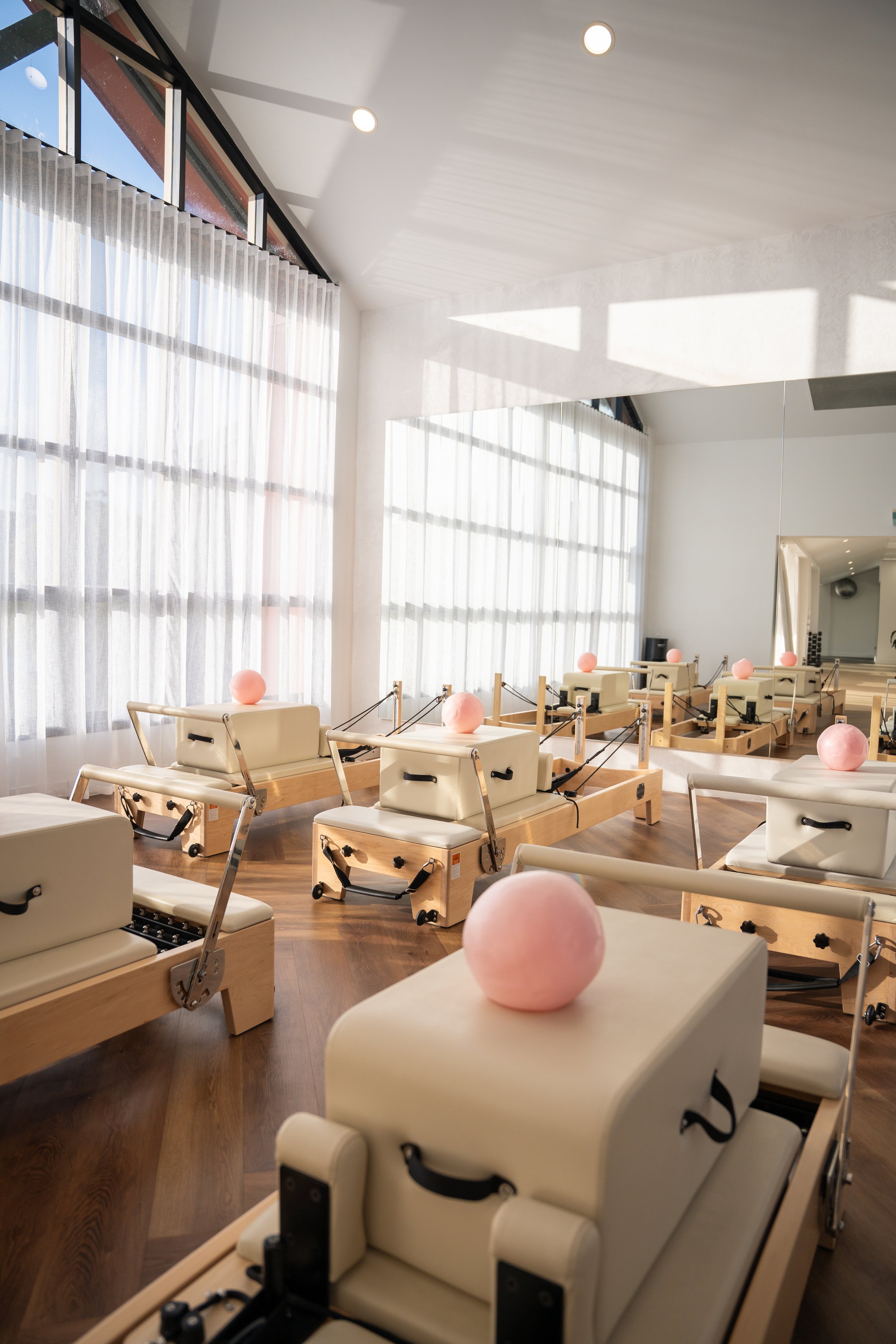 A spacious, modern Pilates studio at Female Physio Co Robina Gold Coast. The room has a wooden floor and a ceiling with recessed lighting, creating a bright and welcoming atmosphere.
